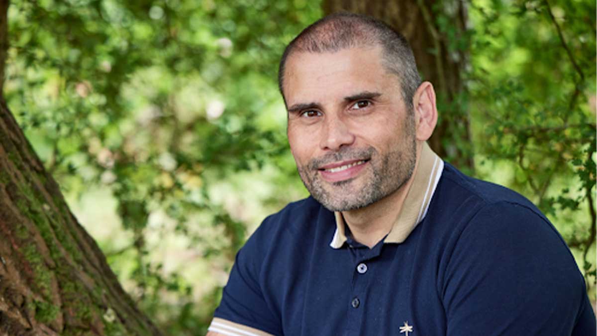 A close up of Harvey sitting by a tree looking at the camera with a smile