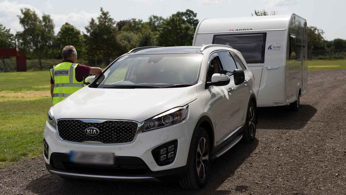 White car towing a caravan with an instructor at the driver's window