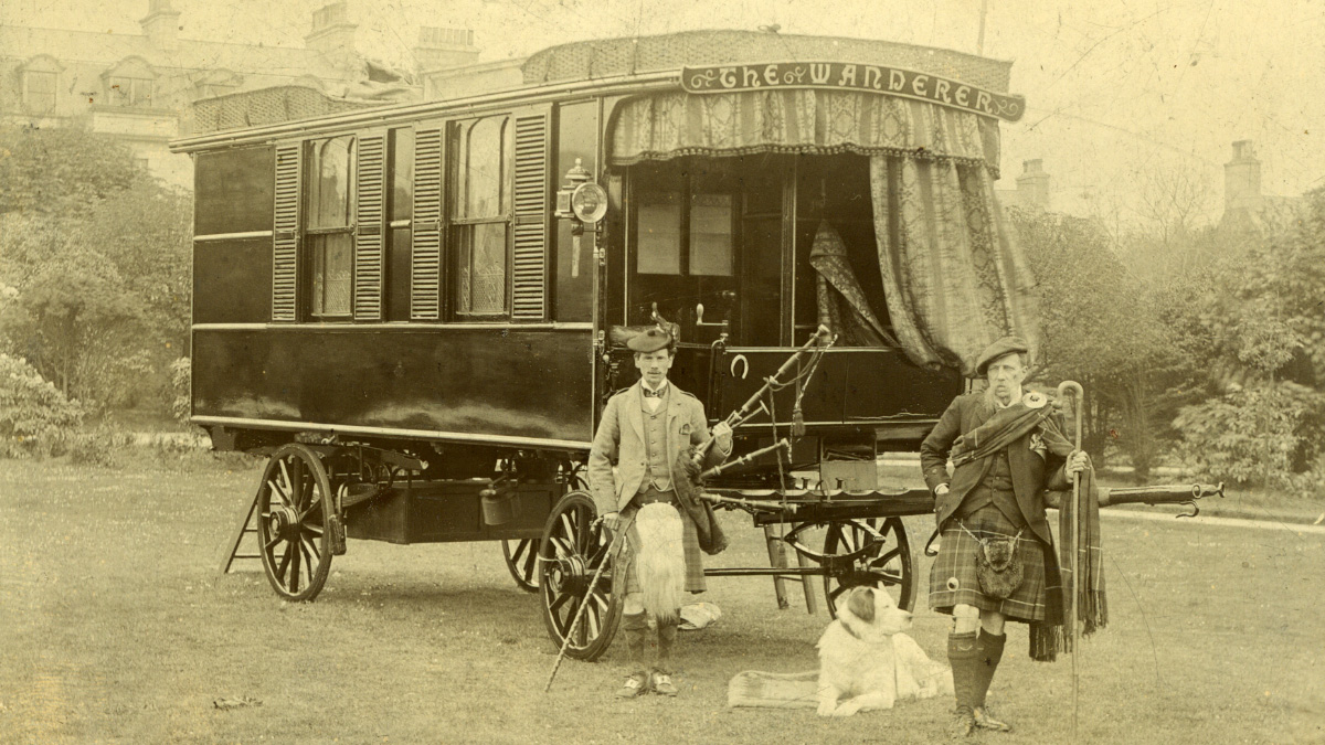 Two people and a dog next to a vintage caravan