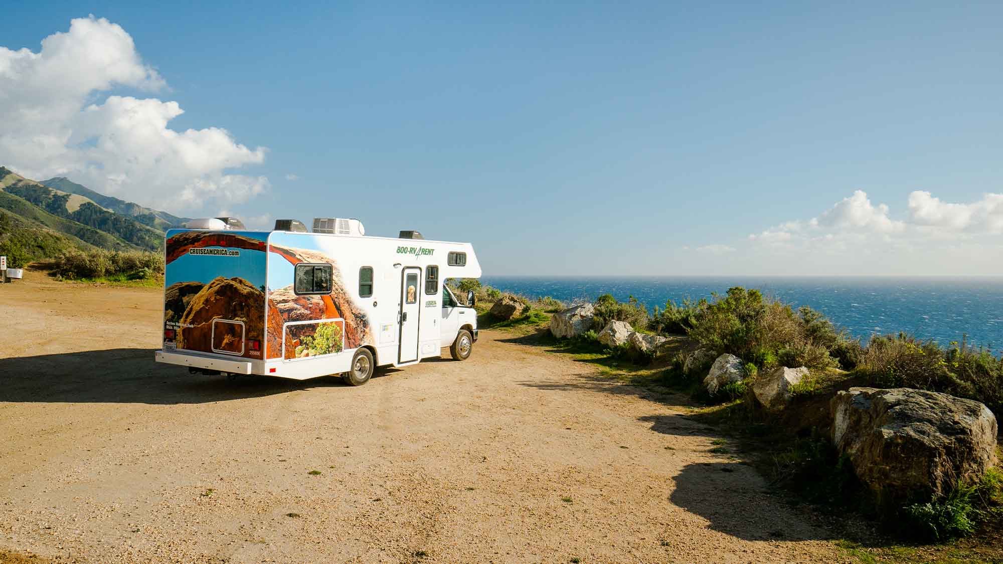 A motorhome parked facing the ocean under a blue sky