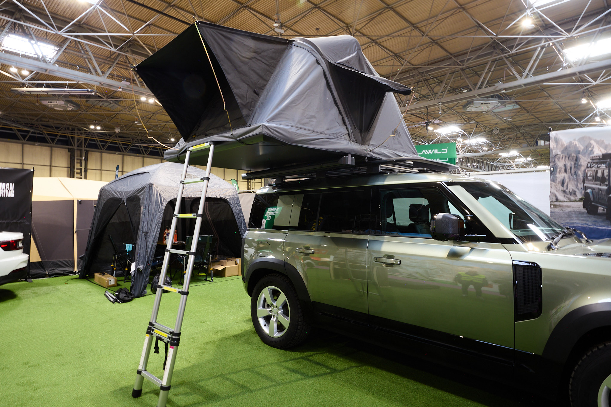 The Roof Space 4 is fully extended on a Land Rover Defender.  The canvas is pale grey, with a black porch.  There is a platform with a sturdy ladder to gain easy access.