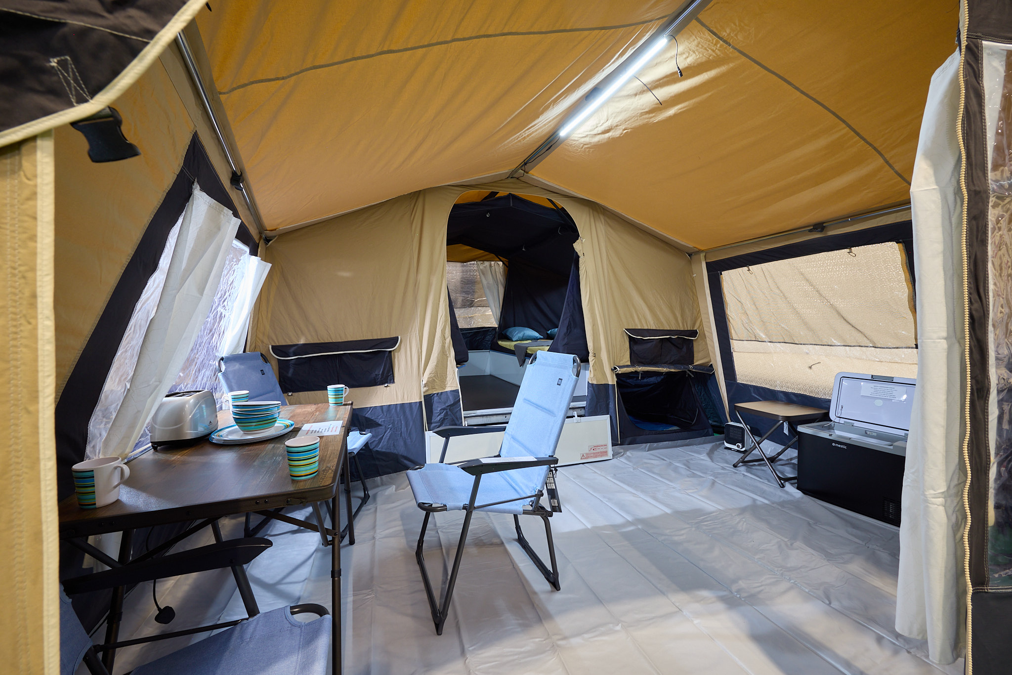 The Trigano Galleon Standard has yellow canvas, there is a cream groundsheet.  There is a step to the bedroom area, there is a dining table and three blue chairs.