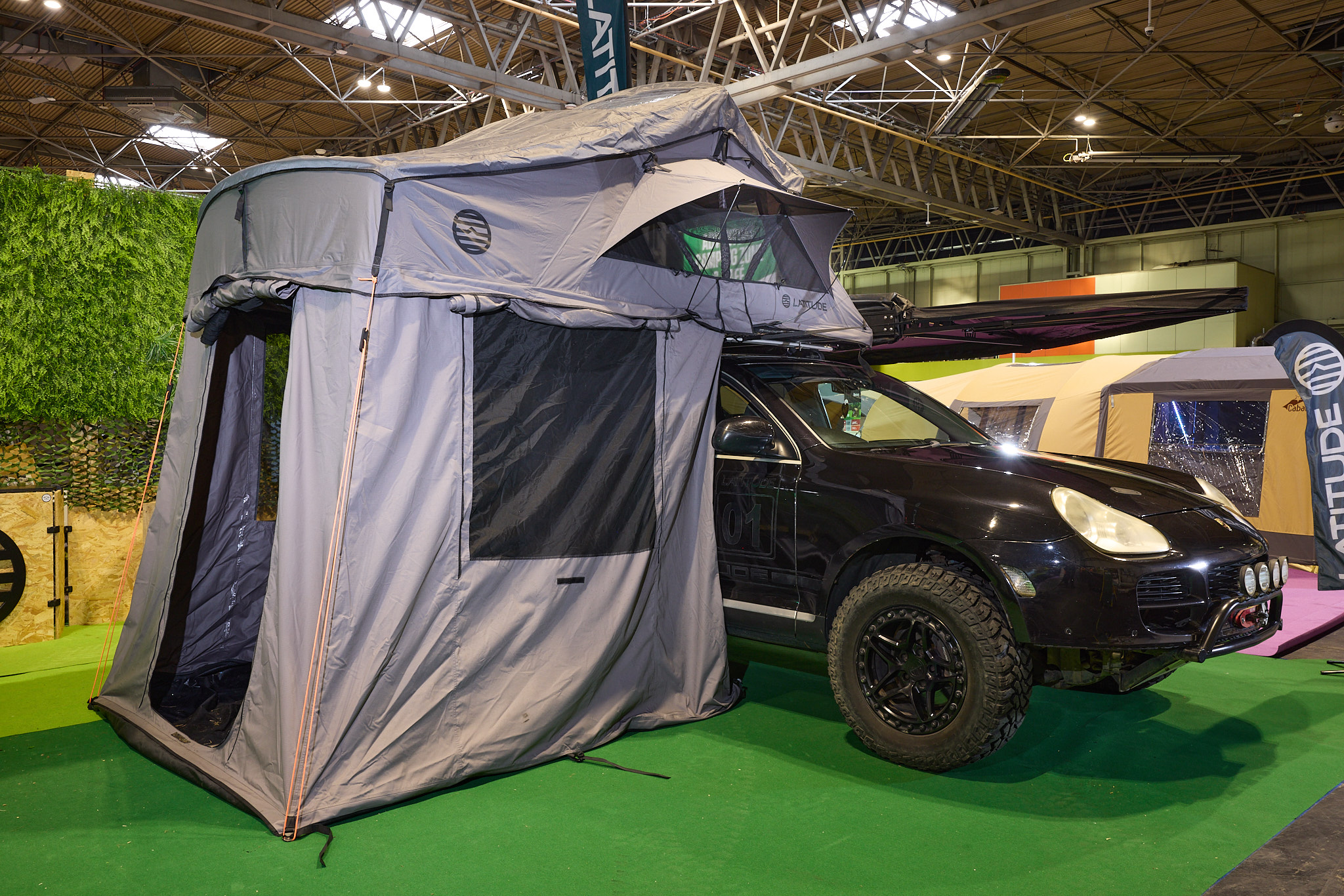 The Latitude Tents Pioneer XL is displayed on a black Porsche.  It has grey canvas walls and a pale grey roof.  It also has an awning.  