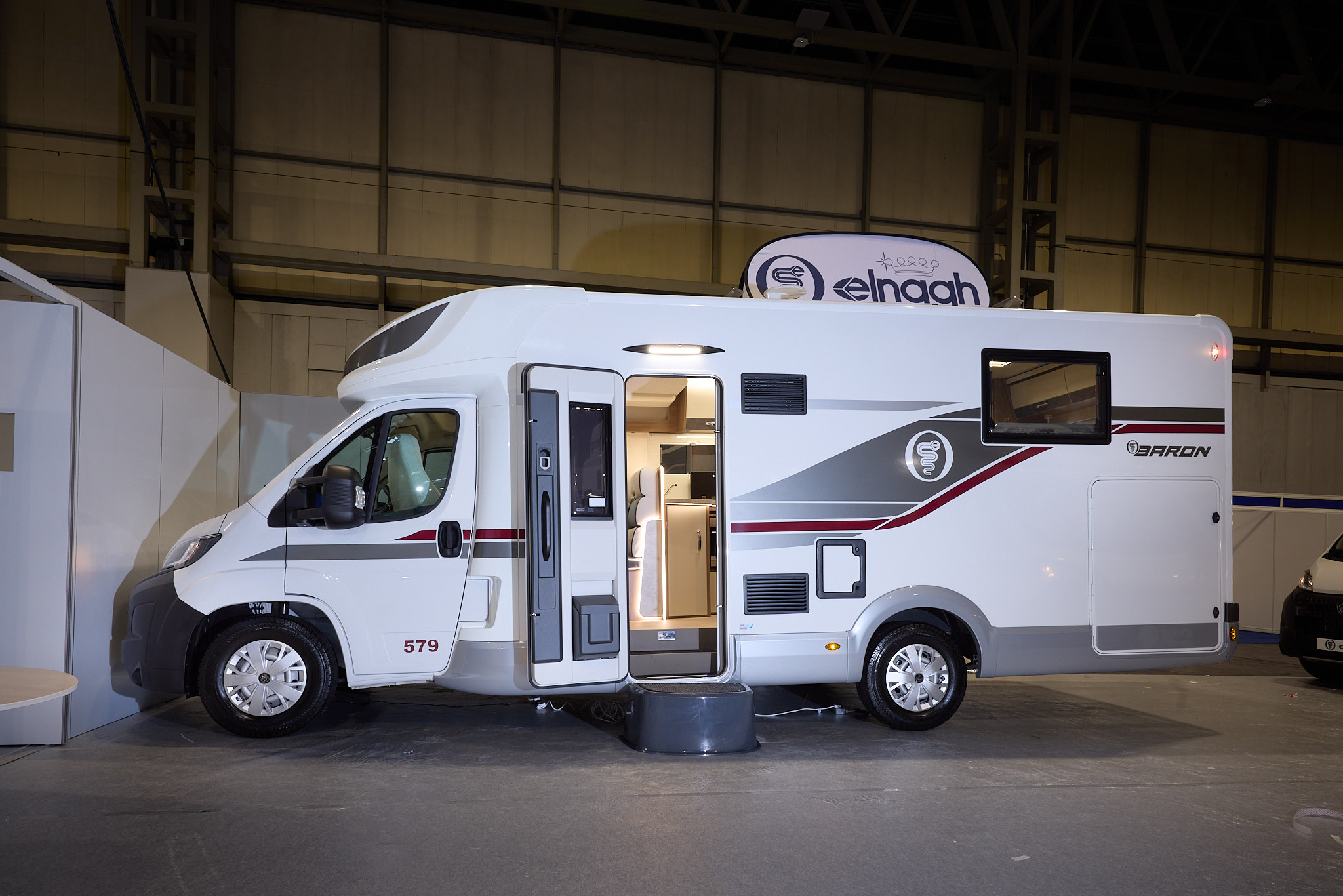 The Elnagh Baron 579 is white with grey and dark red decals.  There is a black step by the open habitation door, revealing the interior.