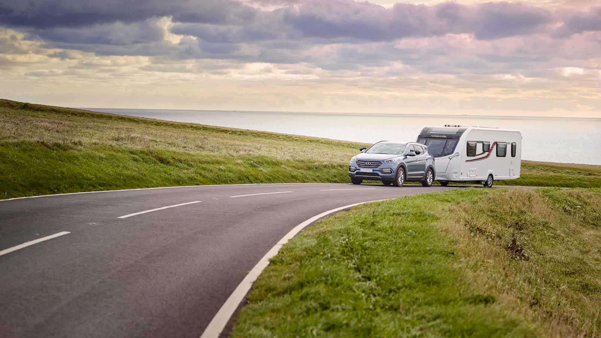 Car towing caravan driving down road surrounded by peaceful scenery