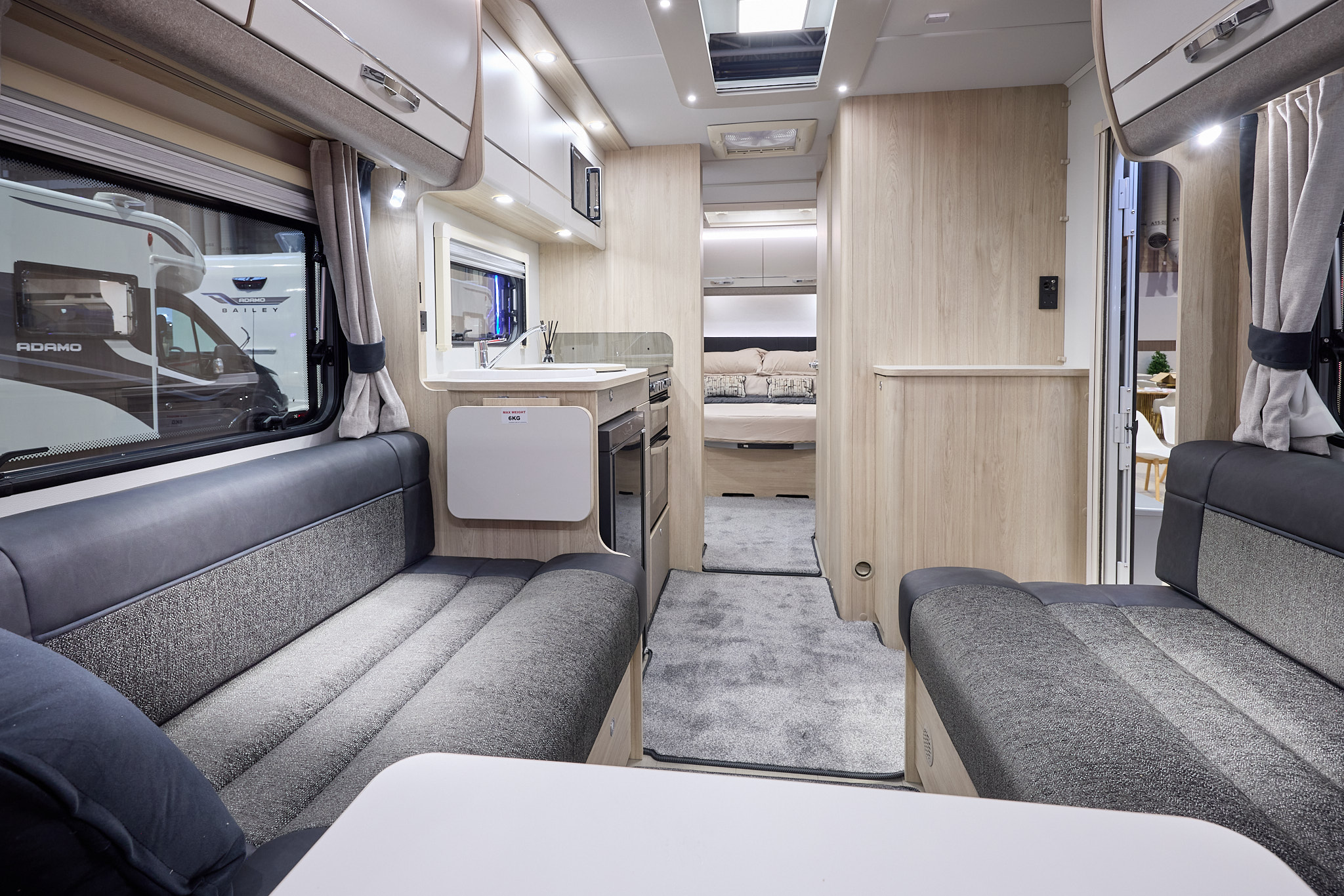 Interior of the Elddis Avanté APEX 550 with dark grey sofas, wood accents and grey carpets.  The large roof light will let natural light flood in.  The rear bedroom door is open.