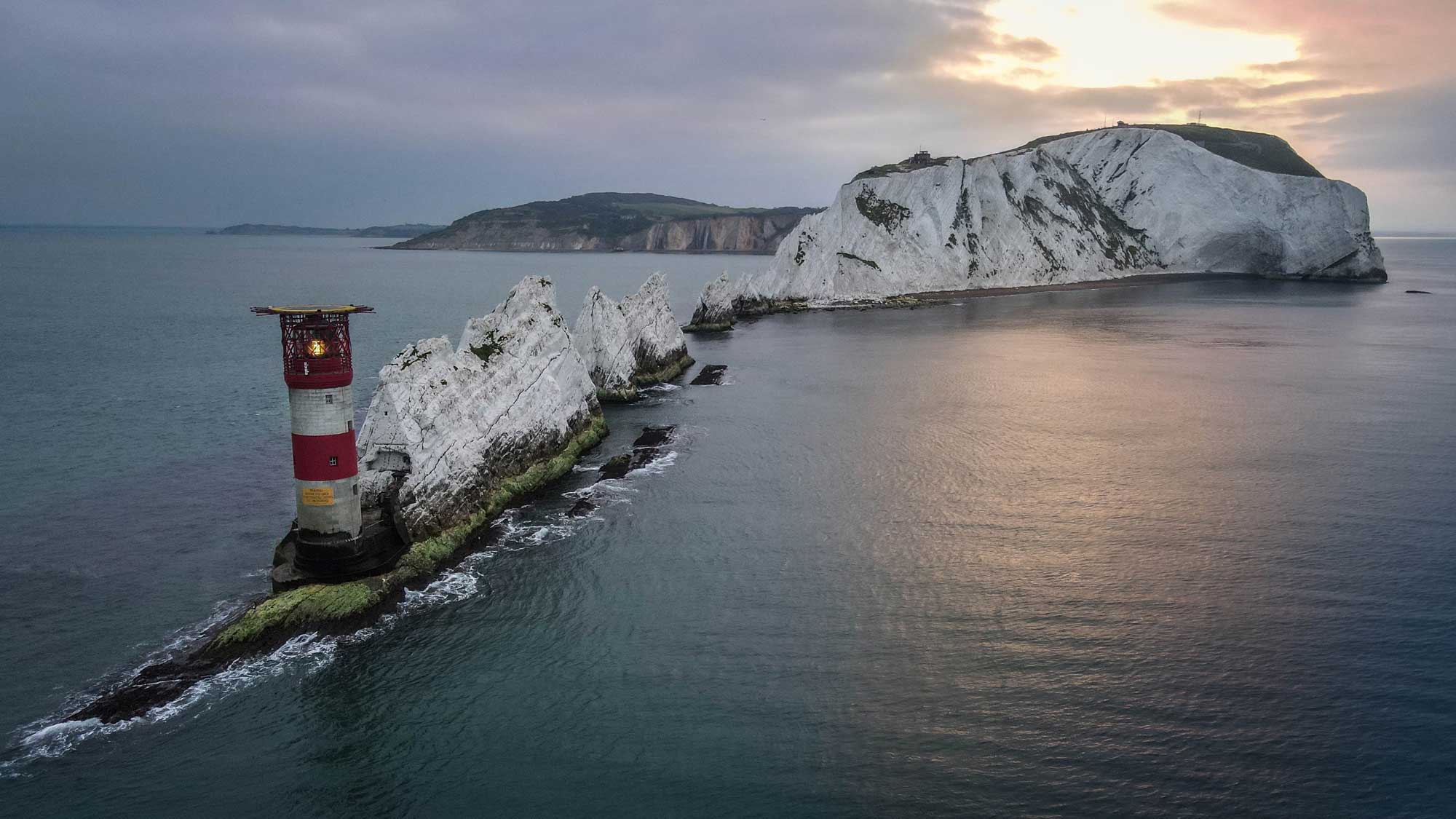a read and white striped lighthouse at the end of the white chalk peaks of the Needles
