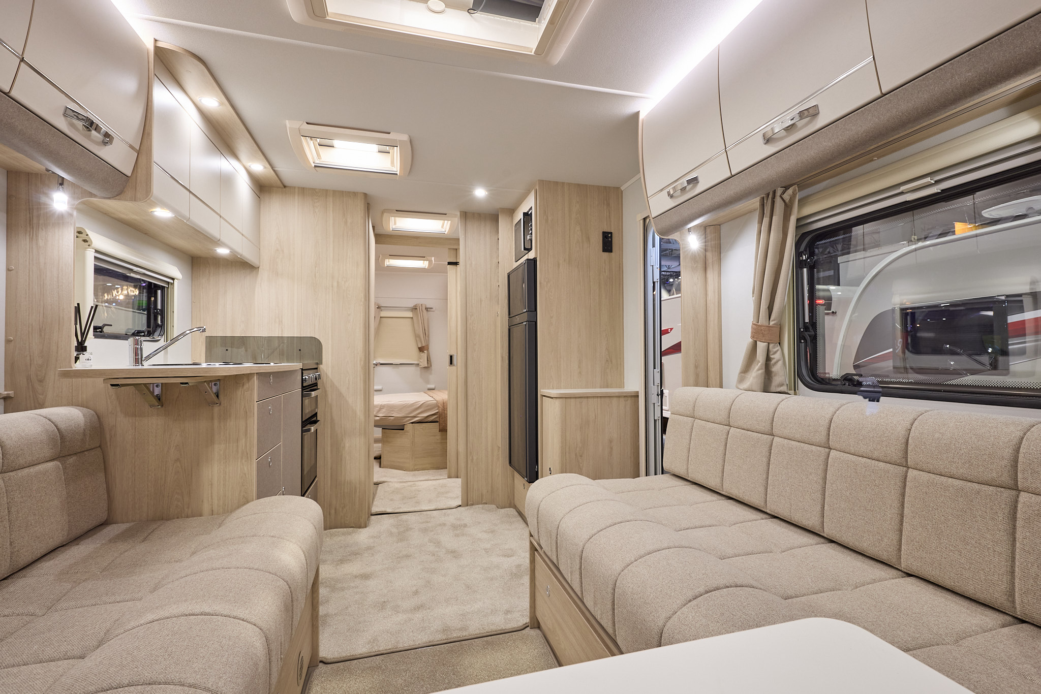 Interior of the Elddis Whirlwind 860 with cream sofas and wood accents and beige carpets. The door to the rear bedroom is open. Perfect for relaxation and designed for comfort.