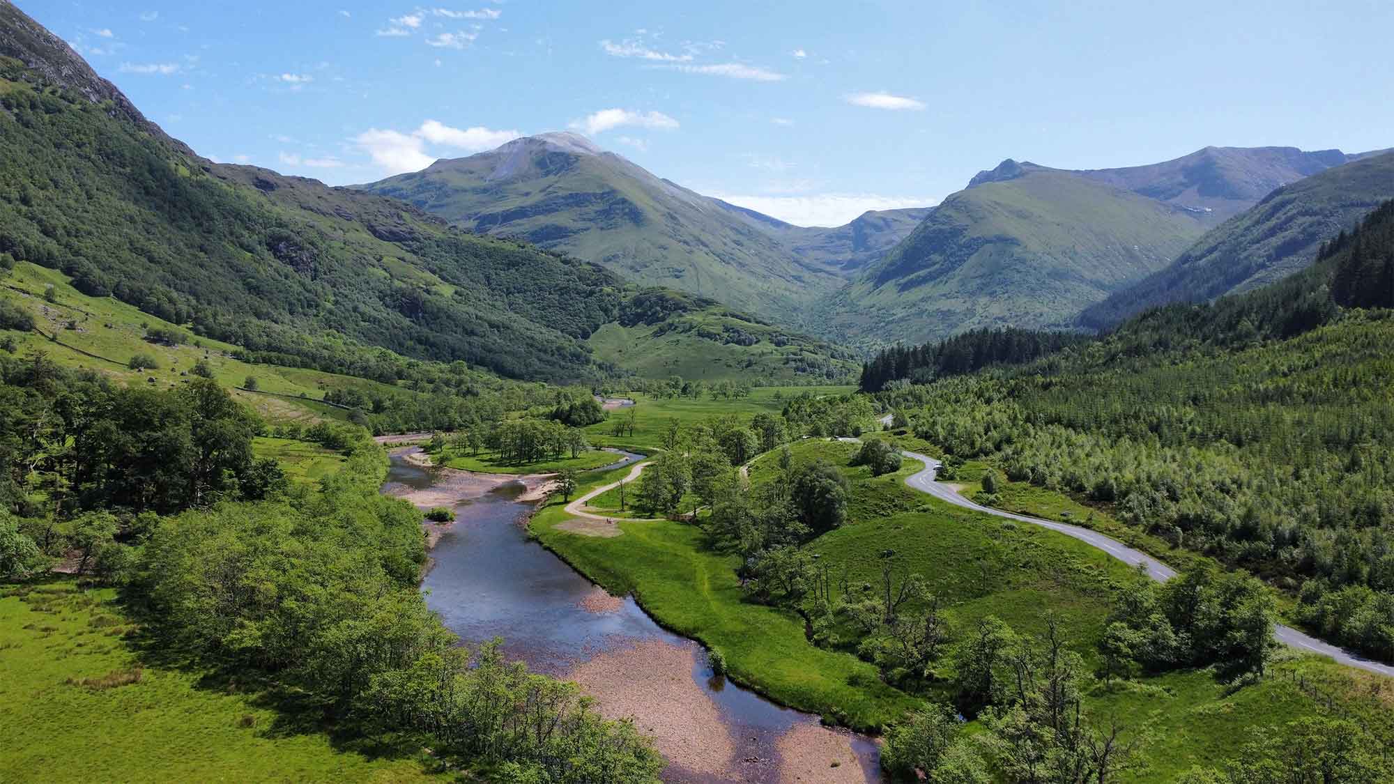 A view from above looking down over the river with is flowing between the grassy mountain slopes 