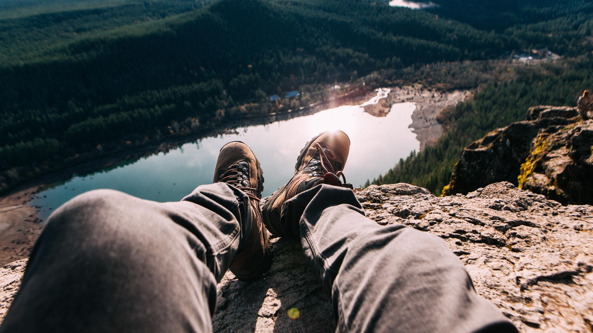 hiker sitting atop cliffside overlooking lake on holiday