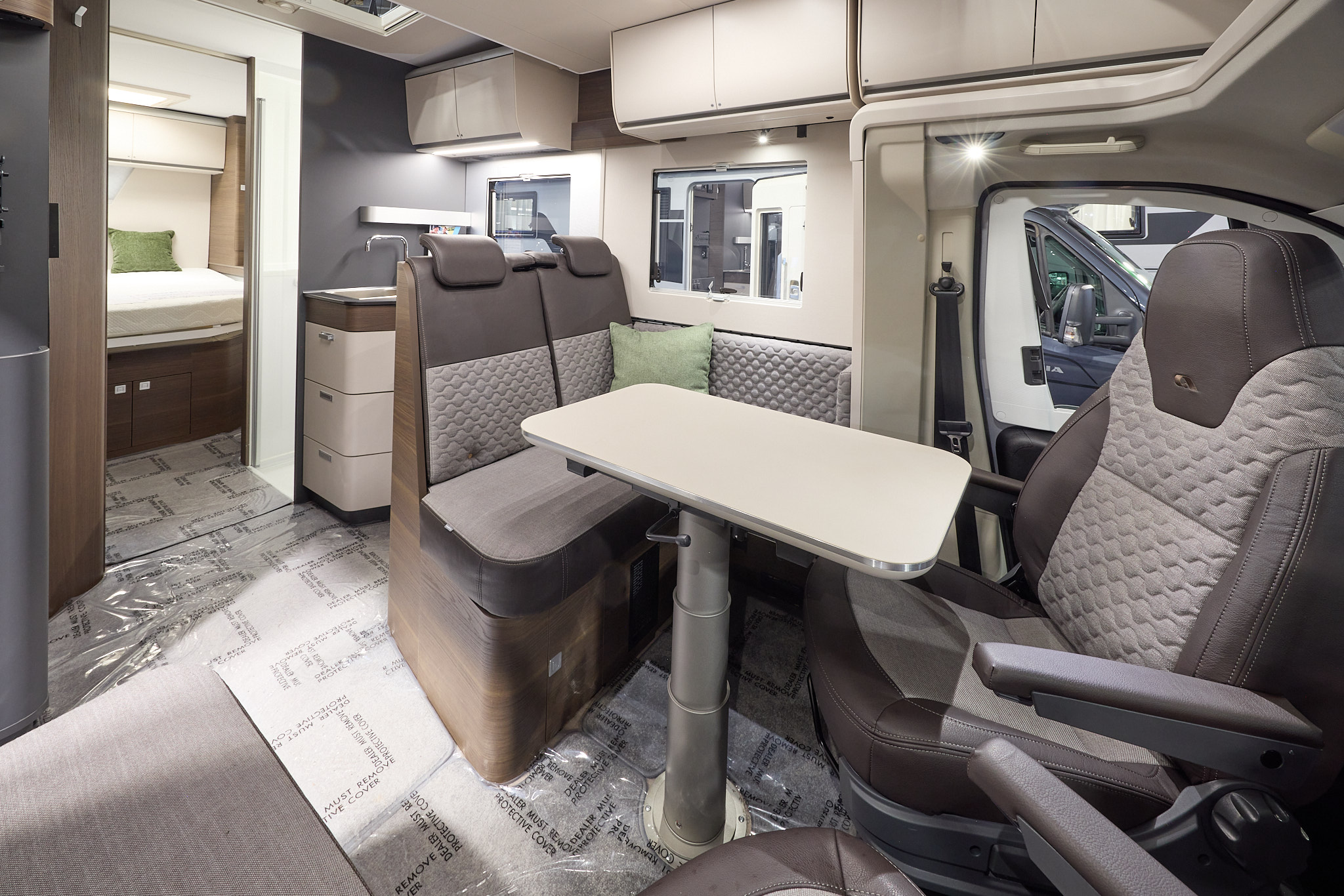 The Adria Matrix Supreme’s floor has protective wrapping, with pale wood cabinets highlighted with darker wood.  The upholstery is two tone with dark edging.  There is a pale wood table, which can be height adjusted.  There is a fixed rear bed.