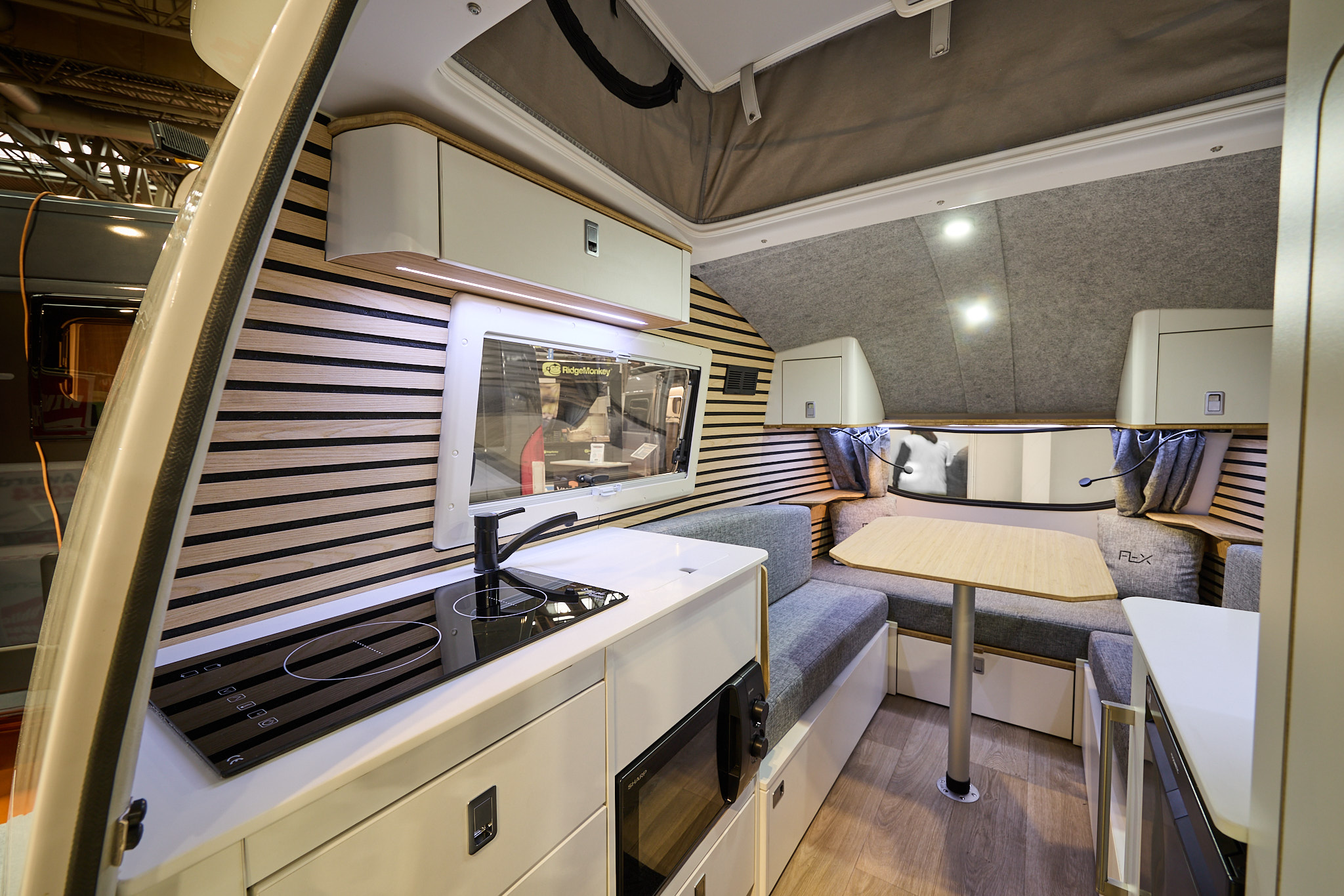 Going Go Pod Flex's interior has cream furniture with grey upholstery.  The walls are covered in slatted wood.  The kitchen is to the right of the entrance door.