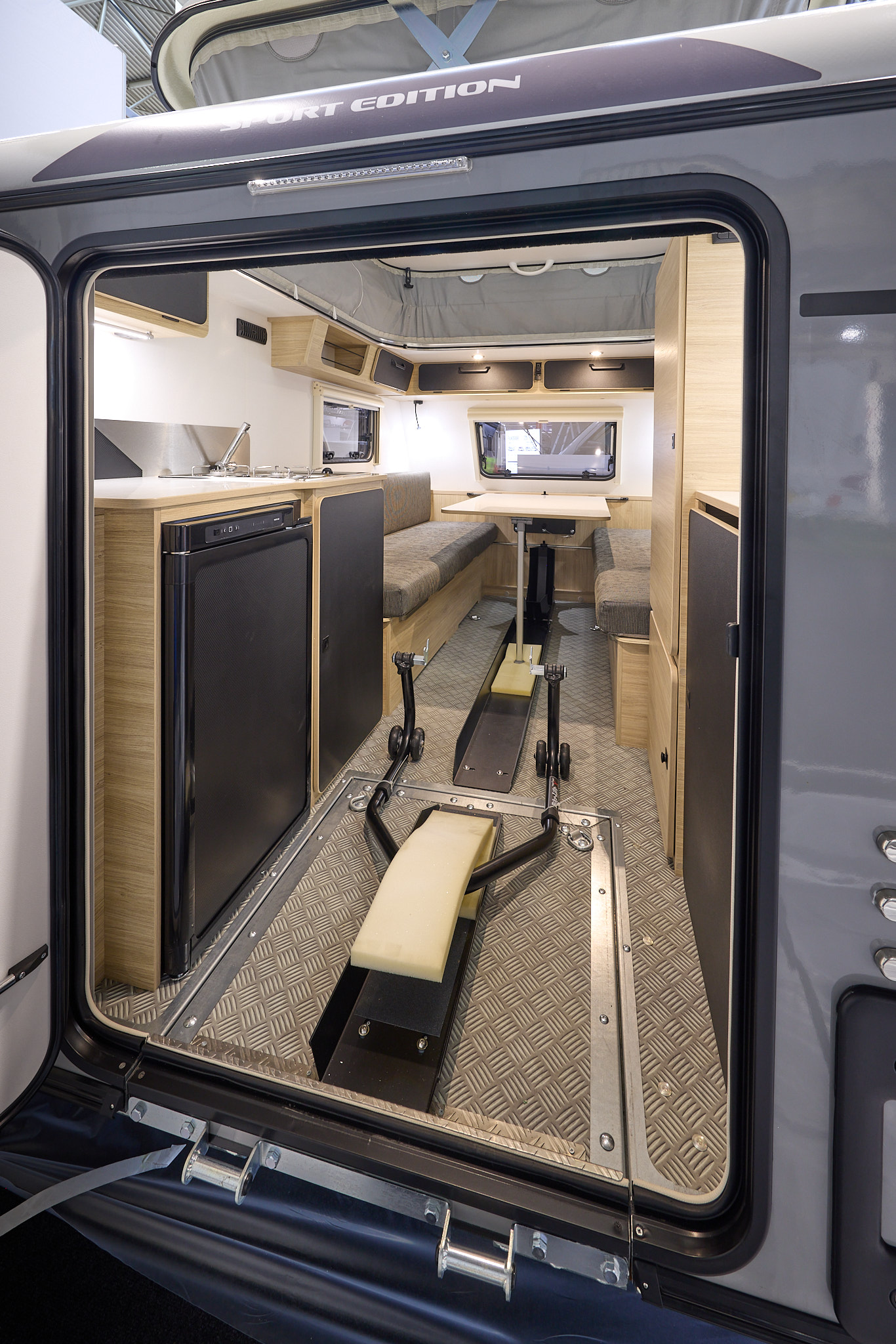 Trigano Mini Freestyle 300 Sport Edition's interior is wooden with the kitchen to the left and the seating area to the front.  There's a bracket on the floor to hold a motorbike whilst travelling