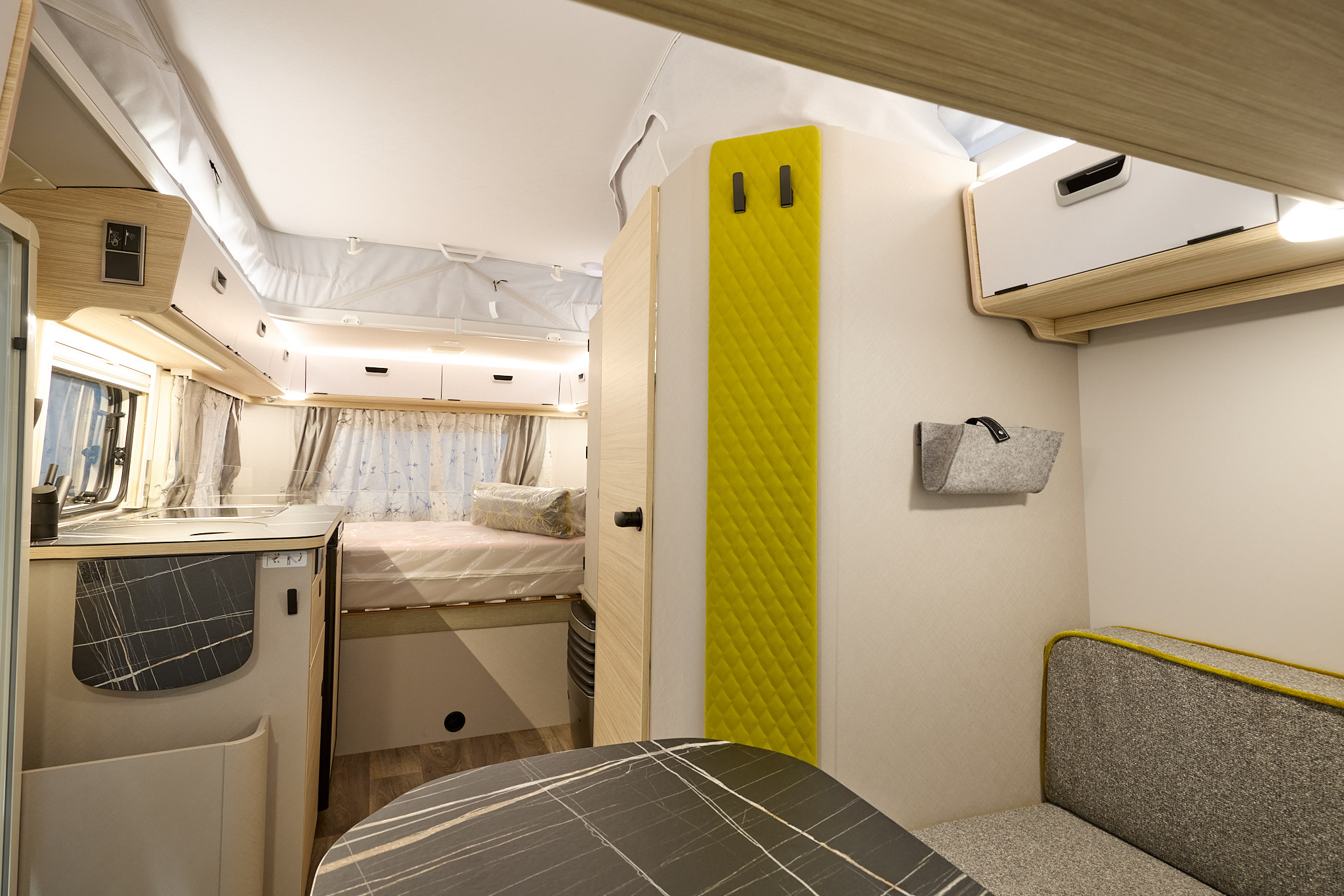 Eriba Touring 530 Nugget Gold Edition’s interior has grey upholstery and its furniture is pale wood.  Thre is a large fixed bed to the rear.  There is a gold panel with two black hooks to the right.