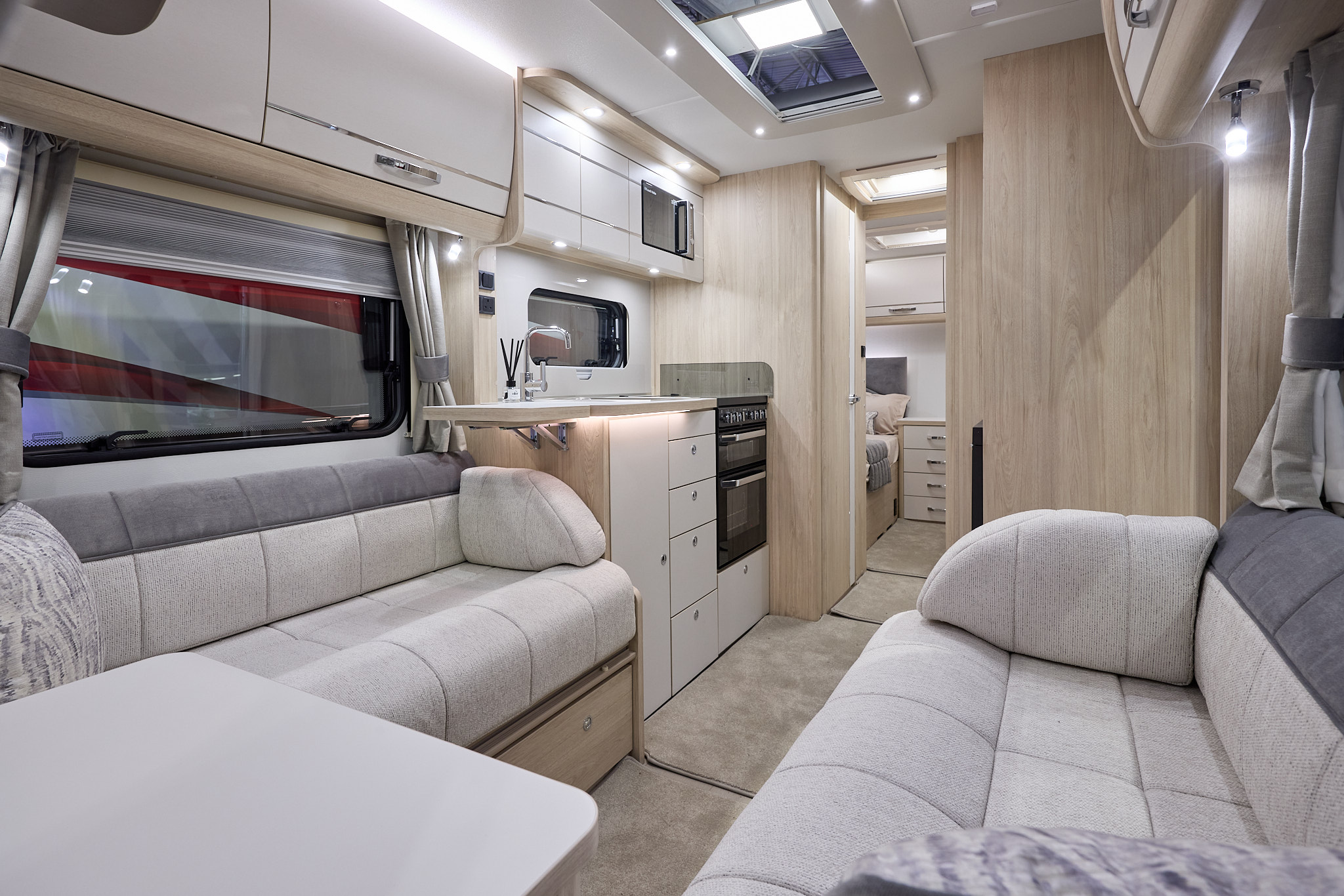 Interior of the Elddis Crusader Shamal with two tone grey sofas, cosy cushions, wood accents and beige carpets.  The door to the rear bedroom is open.  Perfect for relaxation and designed for comfort.