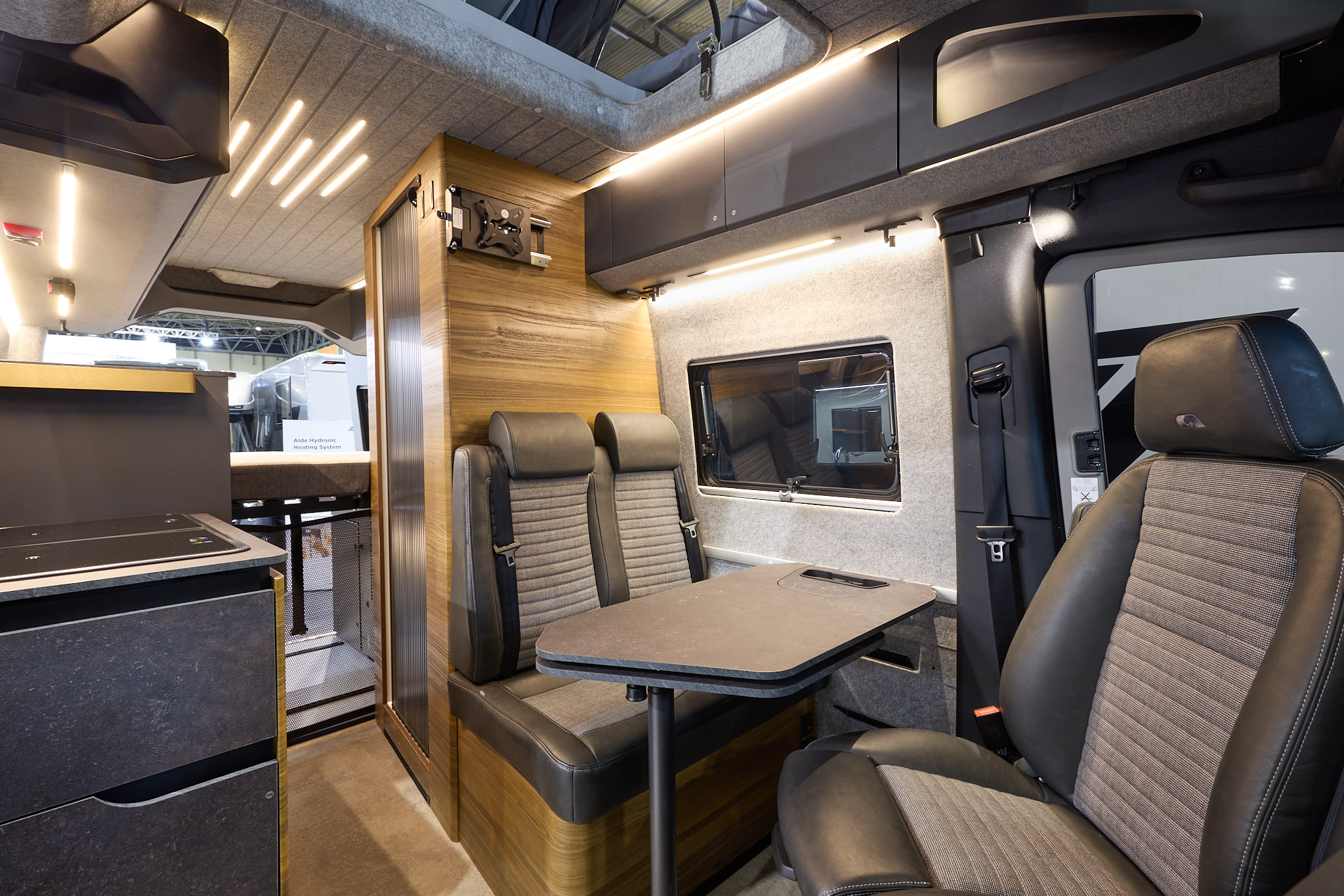 The Adria SuperTwin’s floor is wood effect limo, with dark grey cabinets and wooden panels.  The pop top roof is open and the ceiling is mid grey.  The upholstery is two tone with dark edging.  There is a grey table.