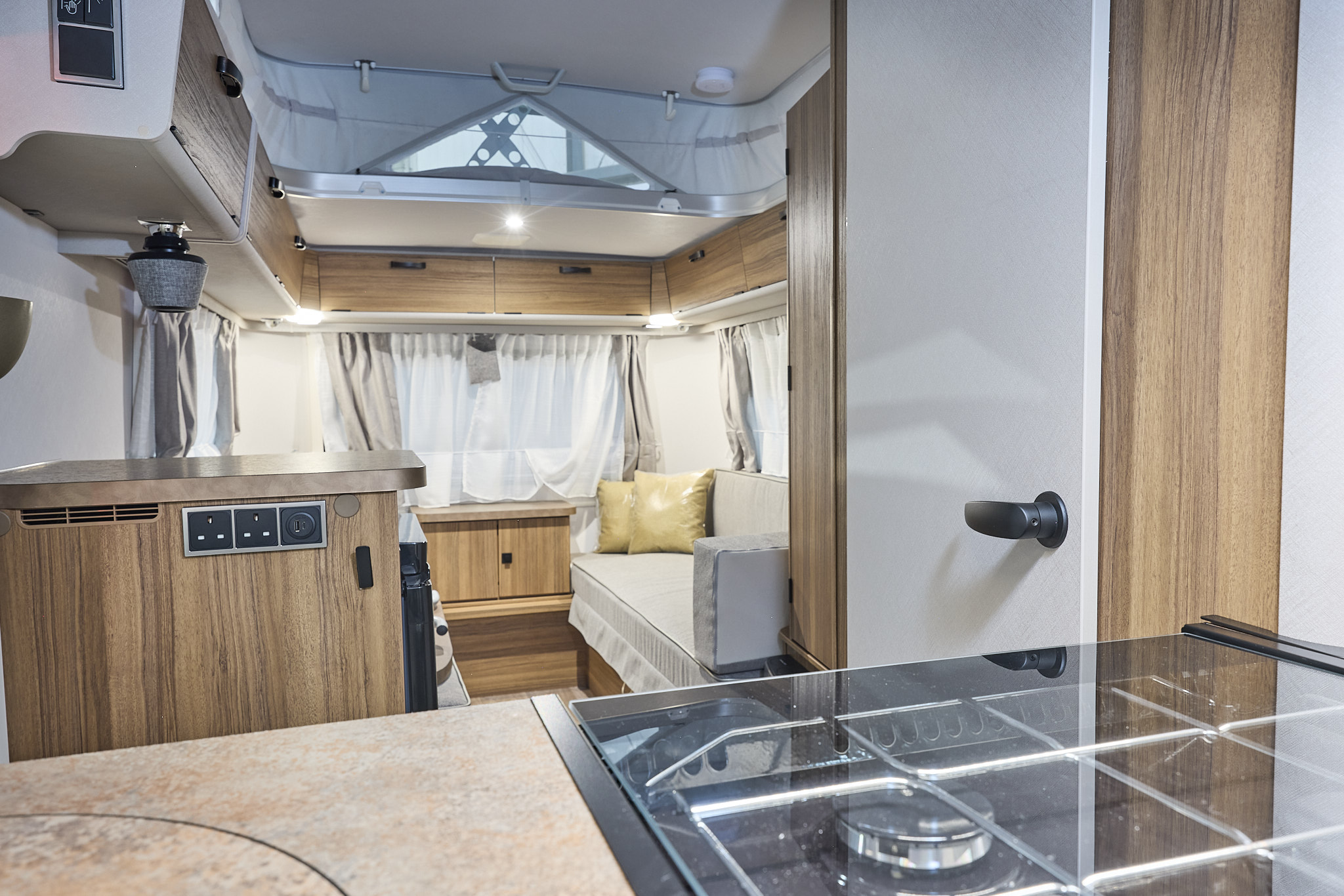 Interior of the Eriba Touring 420 Legend with cream sofas, cushions, wooden accents and a wooden floor.  To the front is the kitchen and its pop top roof is open.