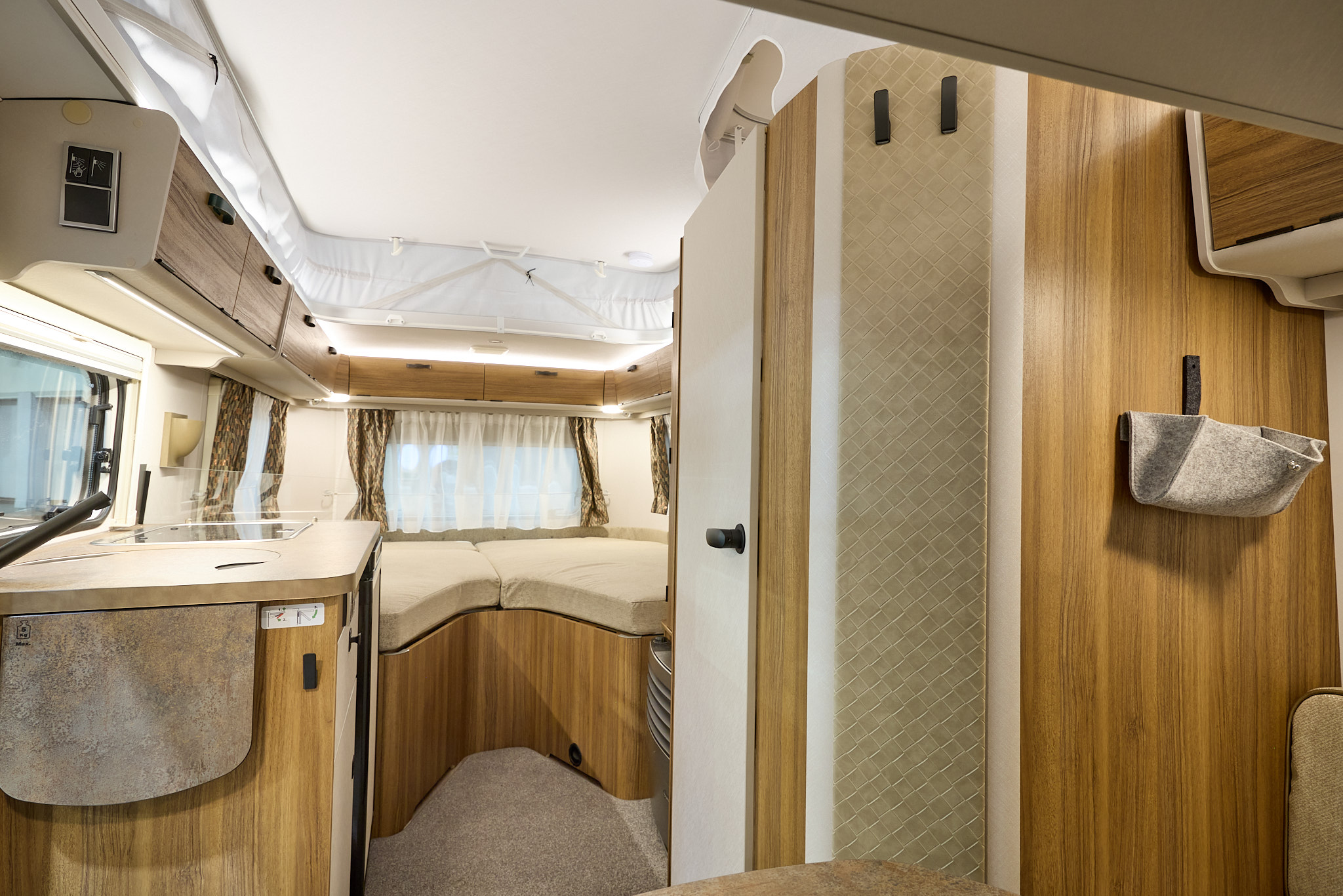 Eriba Touring 542 Legend’s interior has wooden furniture and there is a fixed bed to the rear.  The pop top roof is extended with a white canvas surround.  The handles and wall hooks are black.