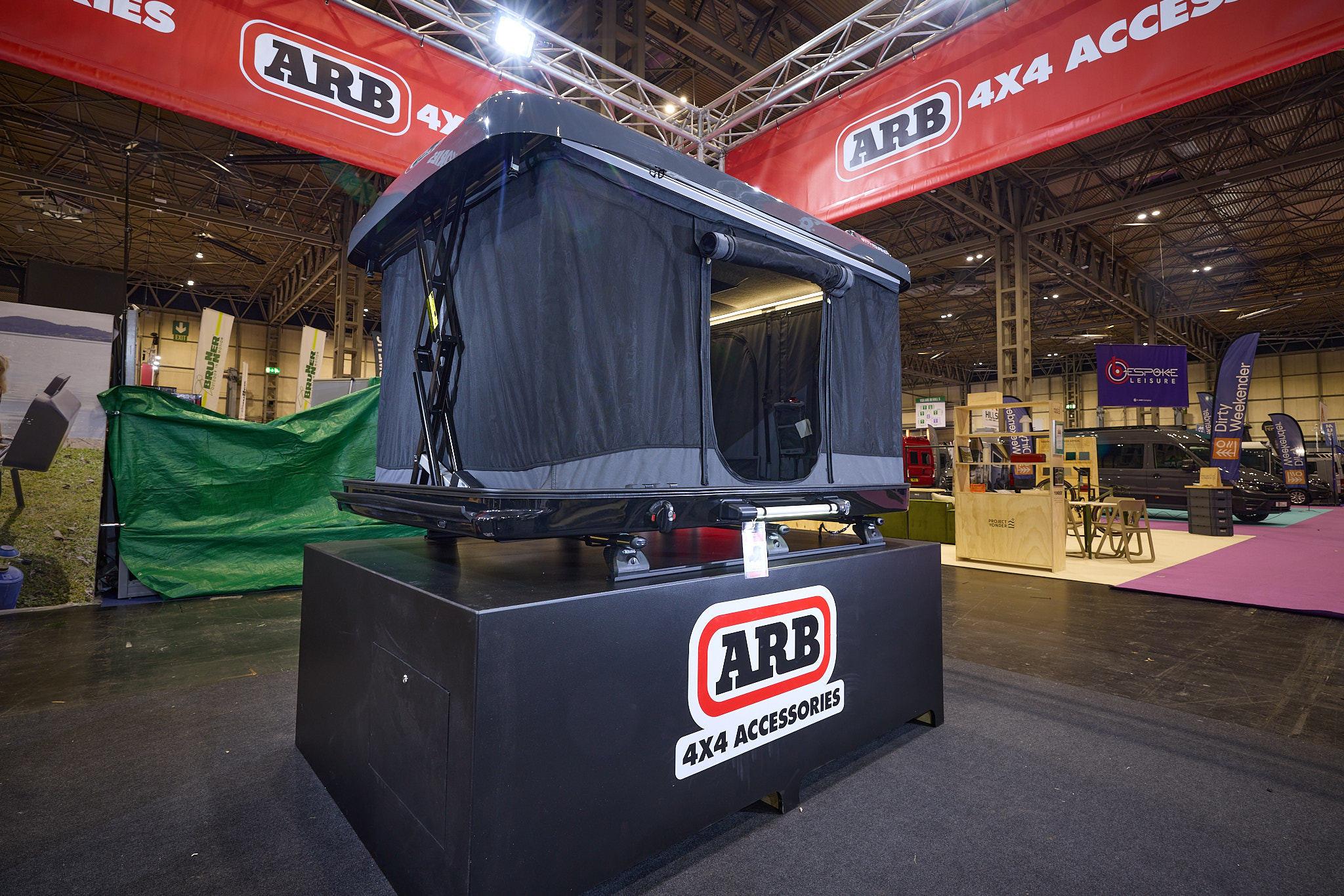 The ARB 4x4 Accessories Altitude is fully extended with two crossed mechanical poles.  It has a solid grey roof and the sides are made of grey canvas.  The door is open, revealing a pocket and a closed window.  The unit is on car roof bars.
