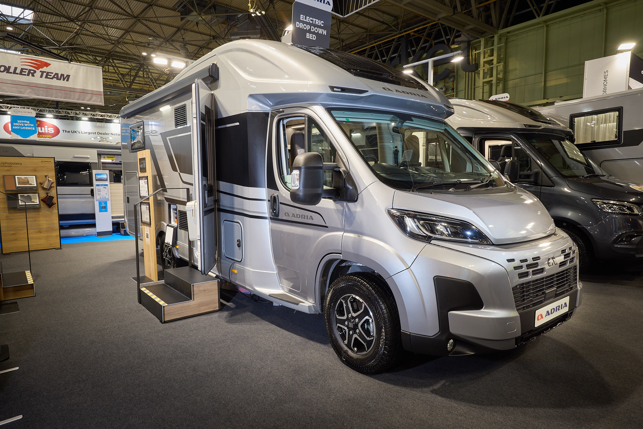 The Adria Matrix Supreme has a silver exterior.  The habitation door is open and there are two steps to gain easy access. There is an information board to the left of the steps.  