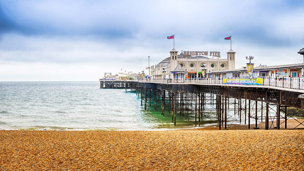 Pebbly beach and Brighton Pier and British flags fluttering in the sea air