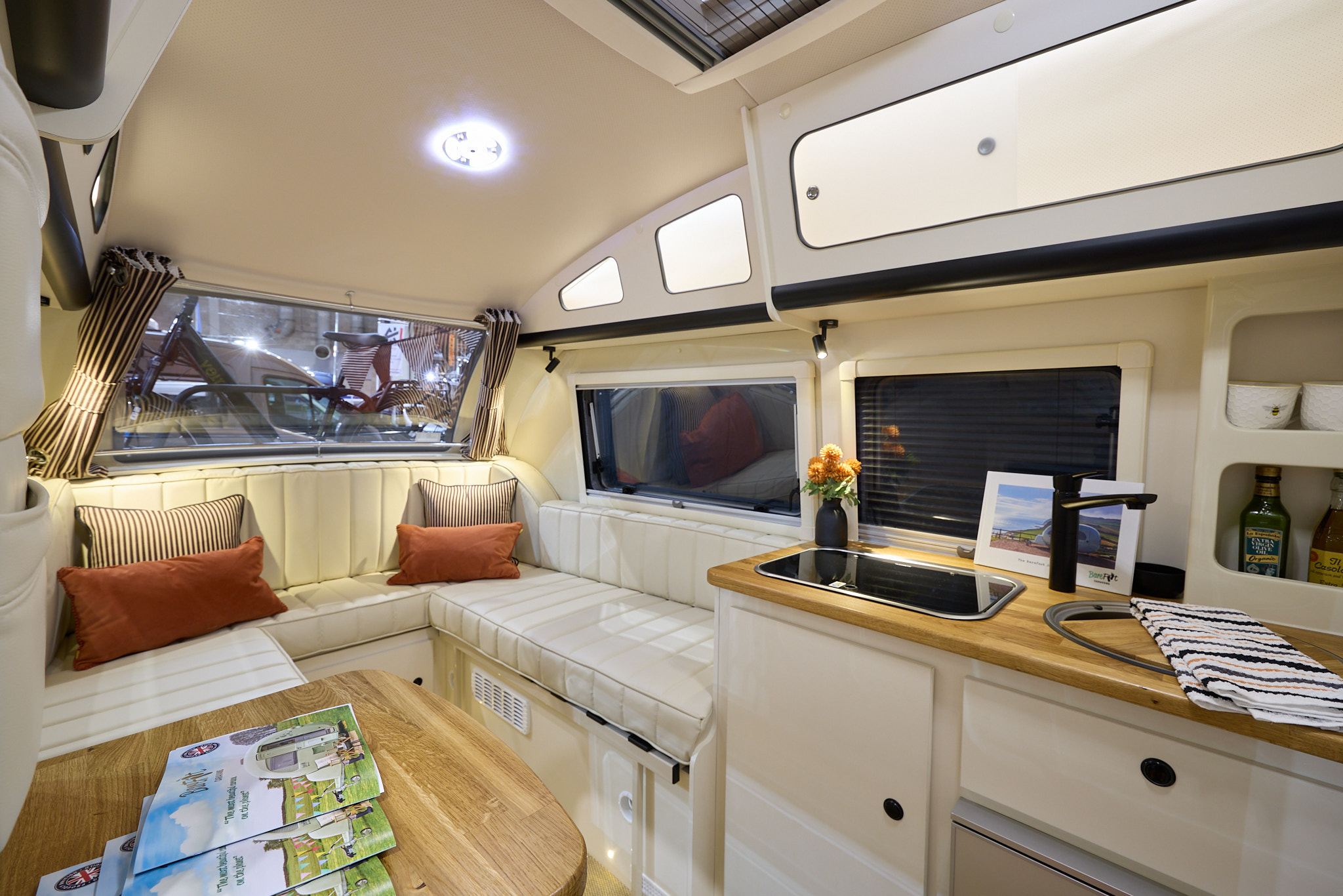 Barefoot Caravan Eclipse’s interior is cream with matching upholstery, there are four cushions on the sofa, two are stripy and two are orange.  There are wooden work surfaces.