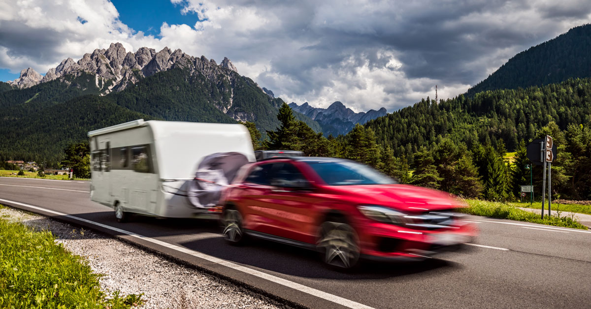red car towing a caravan through mountains
