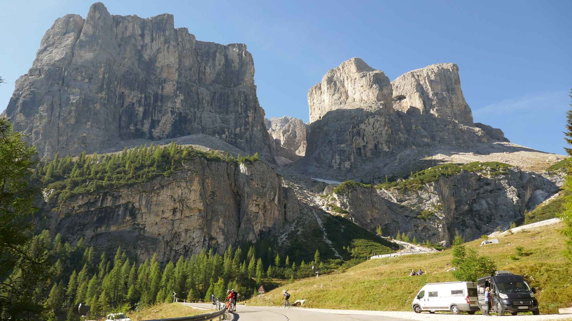 The Dolomites in Italy with motorhomes parked to the side of the winding road leading to the shadows of the huge rock face
