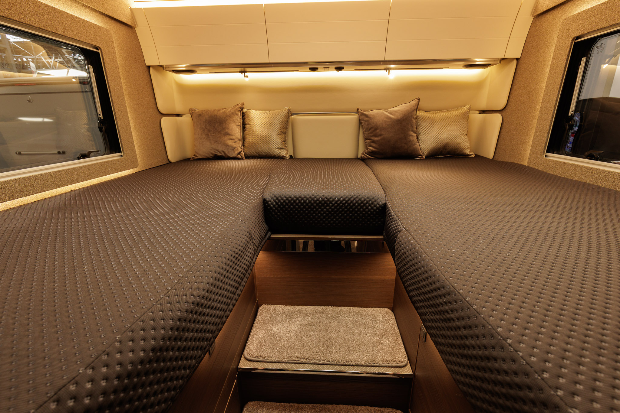 The Adria Supersonic 780 DL has a rear fixed bed.  There are two large windows either side of the bed.  There are four cushions on the bed and there are three cream overhead lockers.  In the front there are two steps to gain entry to the bed.