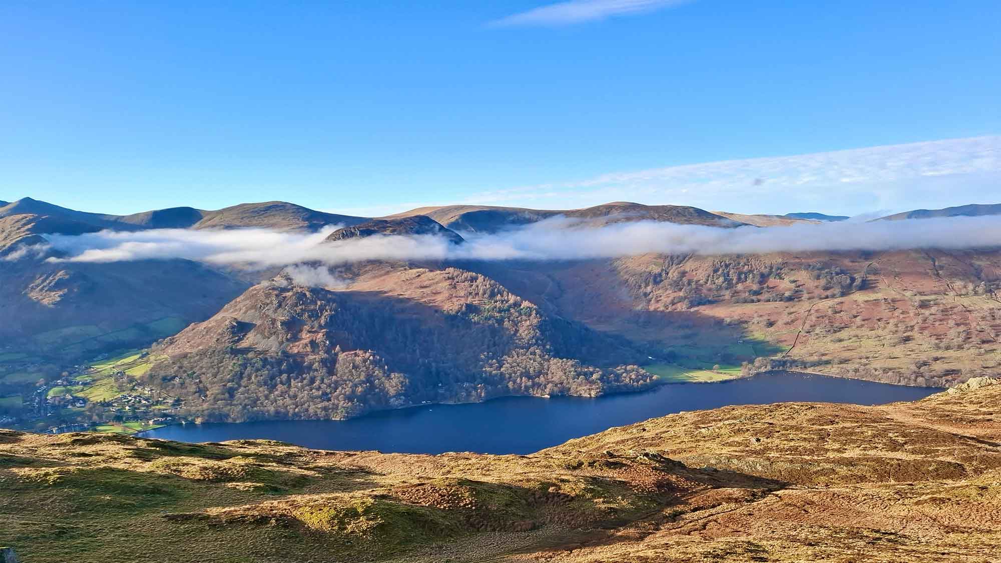 Looking down at Ullswater Lake which is surrounded by hills with a blue-sky backdrop