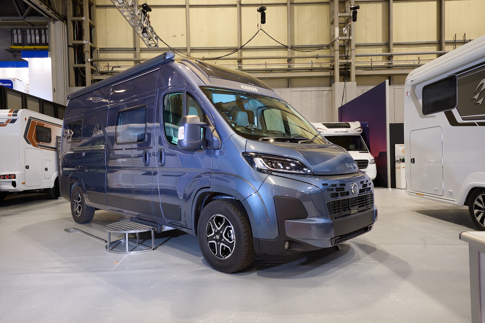 The Knaus Boxlife 600 ME Platinum Selection is blue.  There is a metal step beside the closed sliding door.