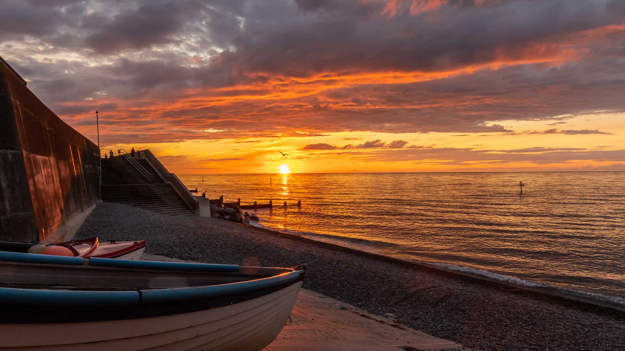 The front of a wooden boat on a beach with a beautiful orange sunset over the sea
