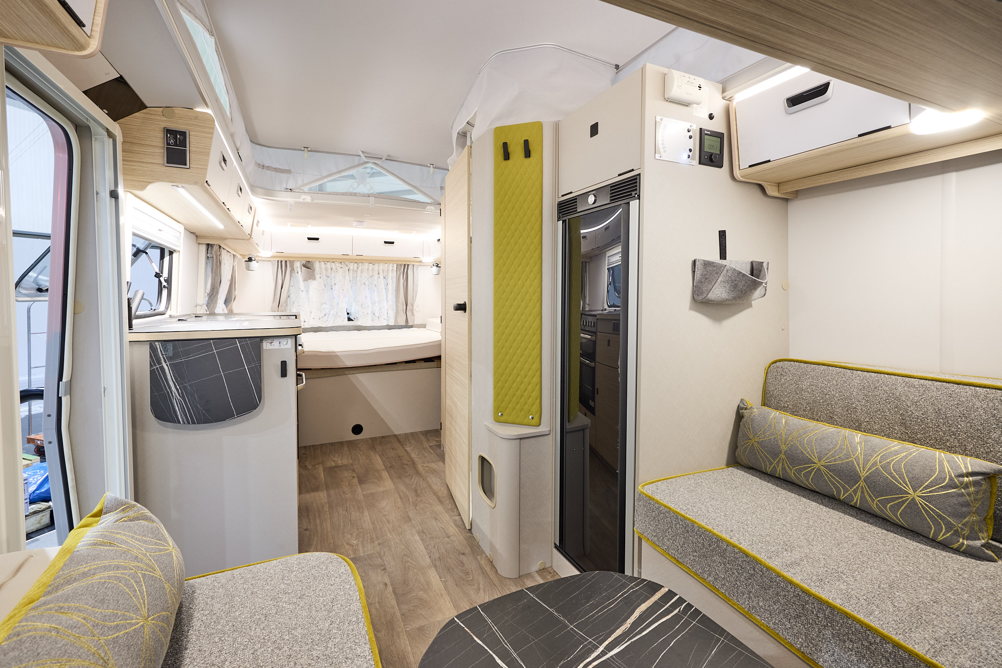 Interior of the Eriba Touring 630 Urban with grey sofas, lime green accents and a wooden floor.  To the rear there is a large fixed bed.