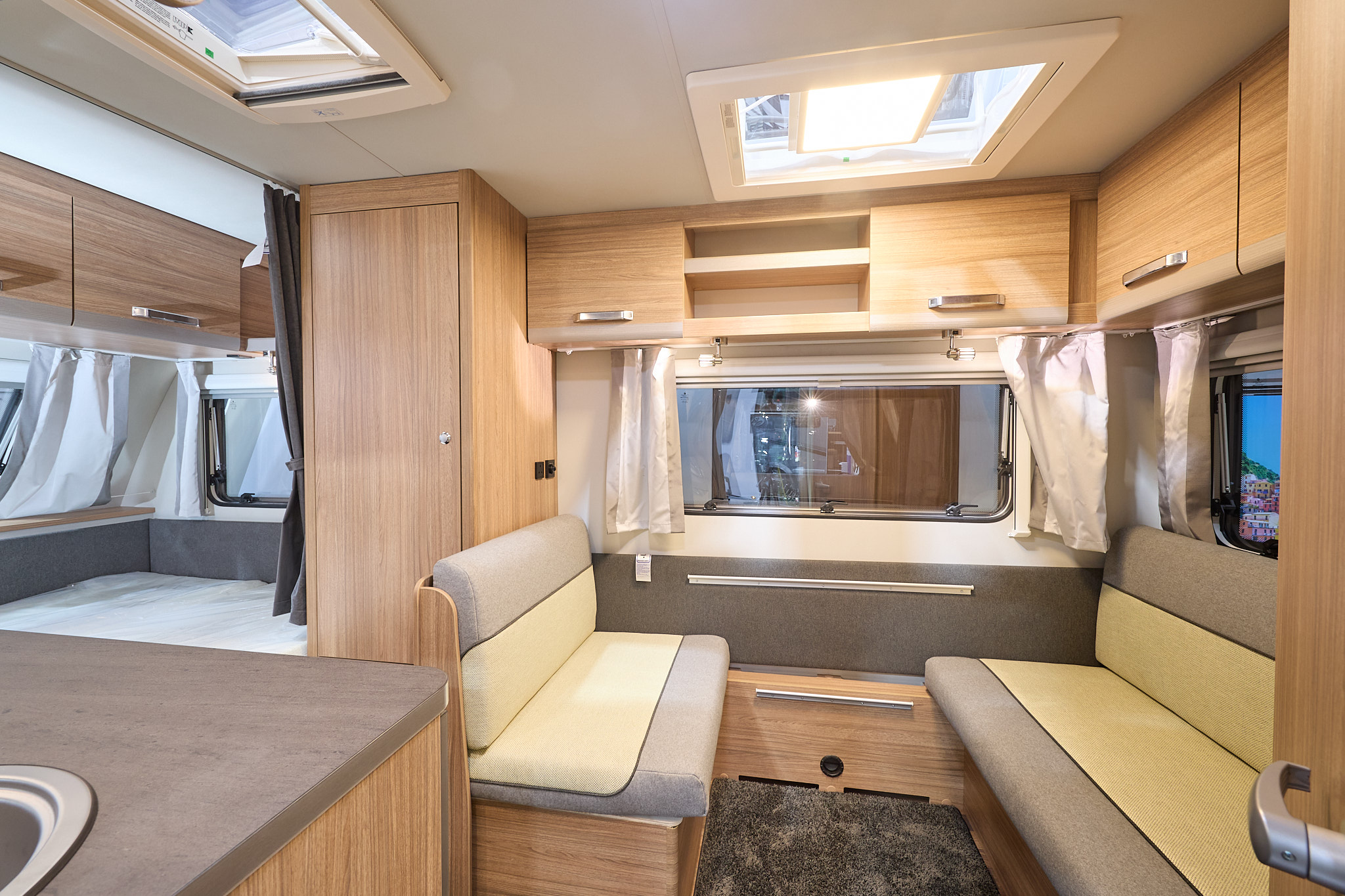 Weinsberg CaraOne 390 QD's interior is primarily wooden with two tone cream and grey seating.  The fixed bed is to the rear.  There are two skylights/