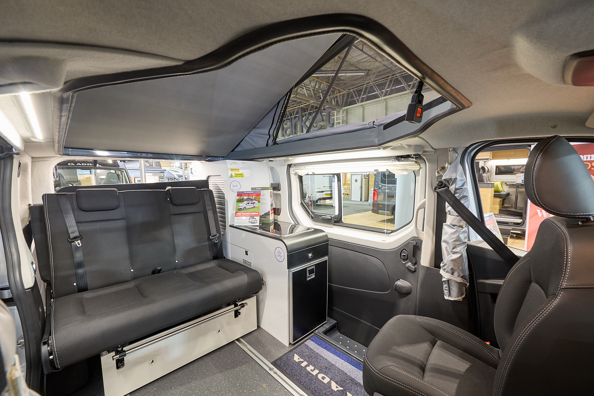 Adria Active Duo's interior has dark grey leather upholstery with white and black units.  The zipped door with access to the roof is partially opened.  The front passenger’s seat is swivelled.