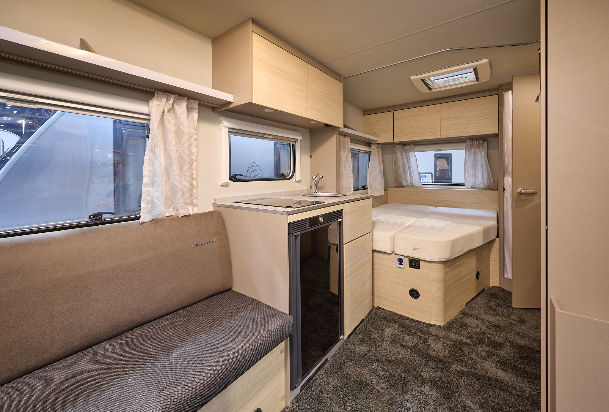 Weinsberg CaraCito 450 FU's interior is primarily wooden with two tone brown seating.  The fixed bed is to the rear.  There is a patterned carpet.