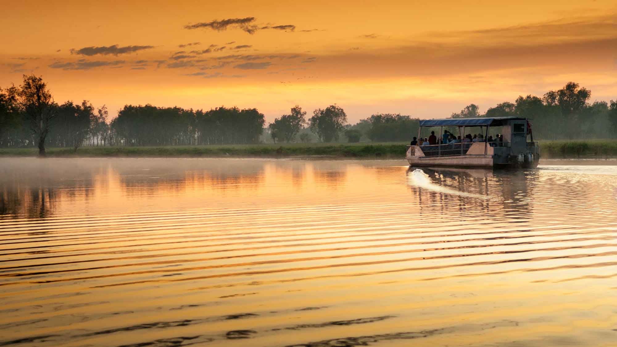 A boat on the calm waters  of Yellow Water Billabong under an amazing golden sky in Kakadu National Park Australia