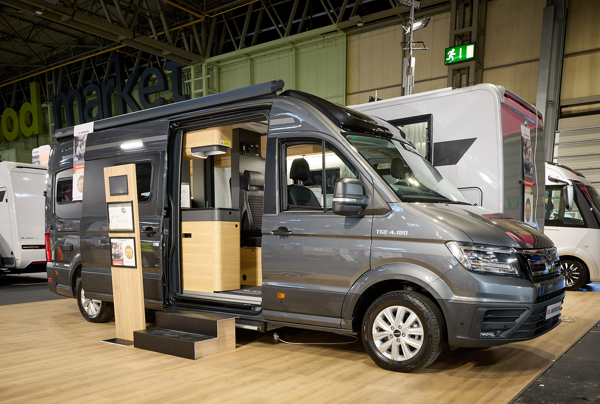 Adria Twin Max’s exterior is dark grey, the sliding door is open and there are wooden steps to gain easy access.  There is an interactive information board by the side of the van.