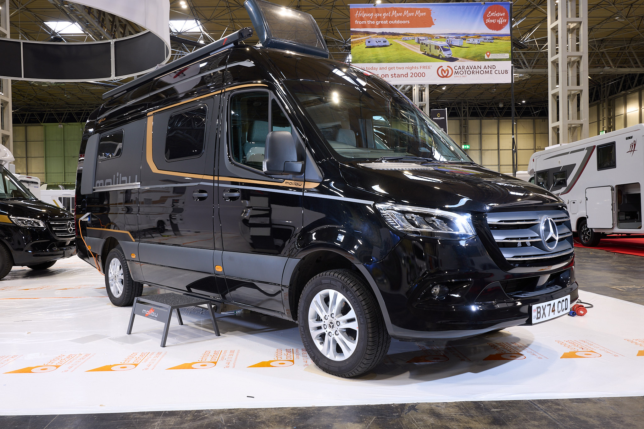The Malibu Genius 641 LE is black with gold decals.  There is a black step by the slding habitation door.  The front sunroof is open, as are the rear doors.