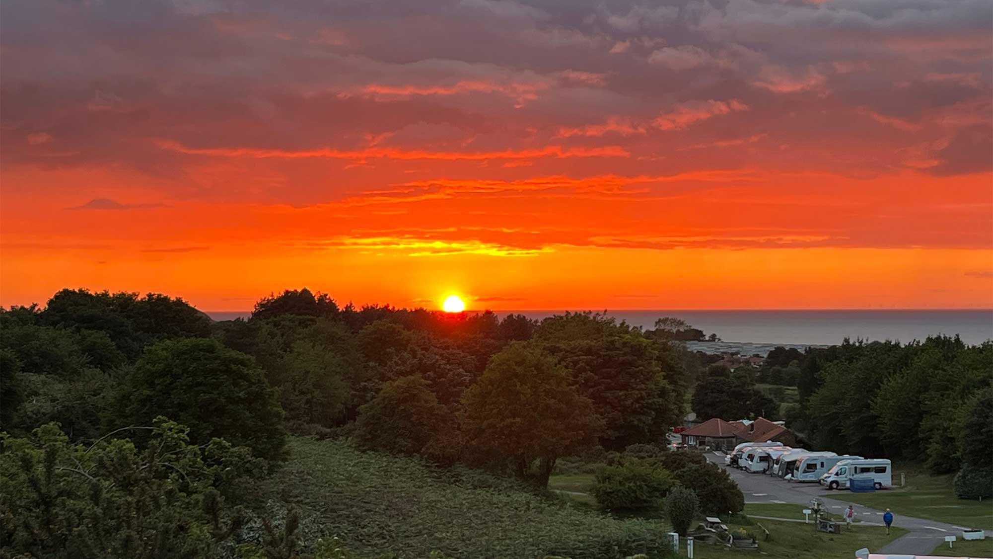 An amazing sunset in a dark orange sky with a view of caravans and trees