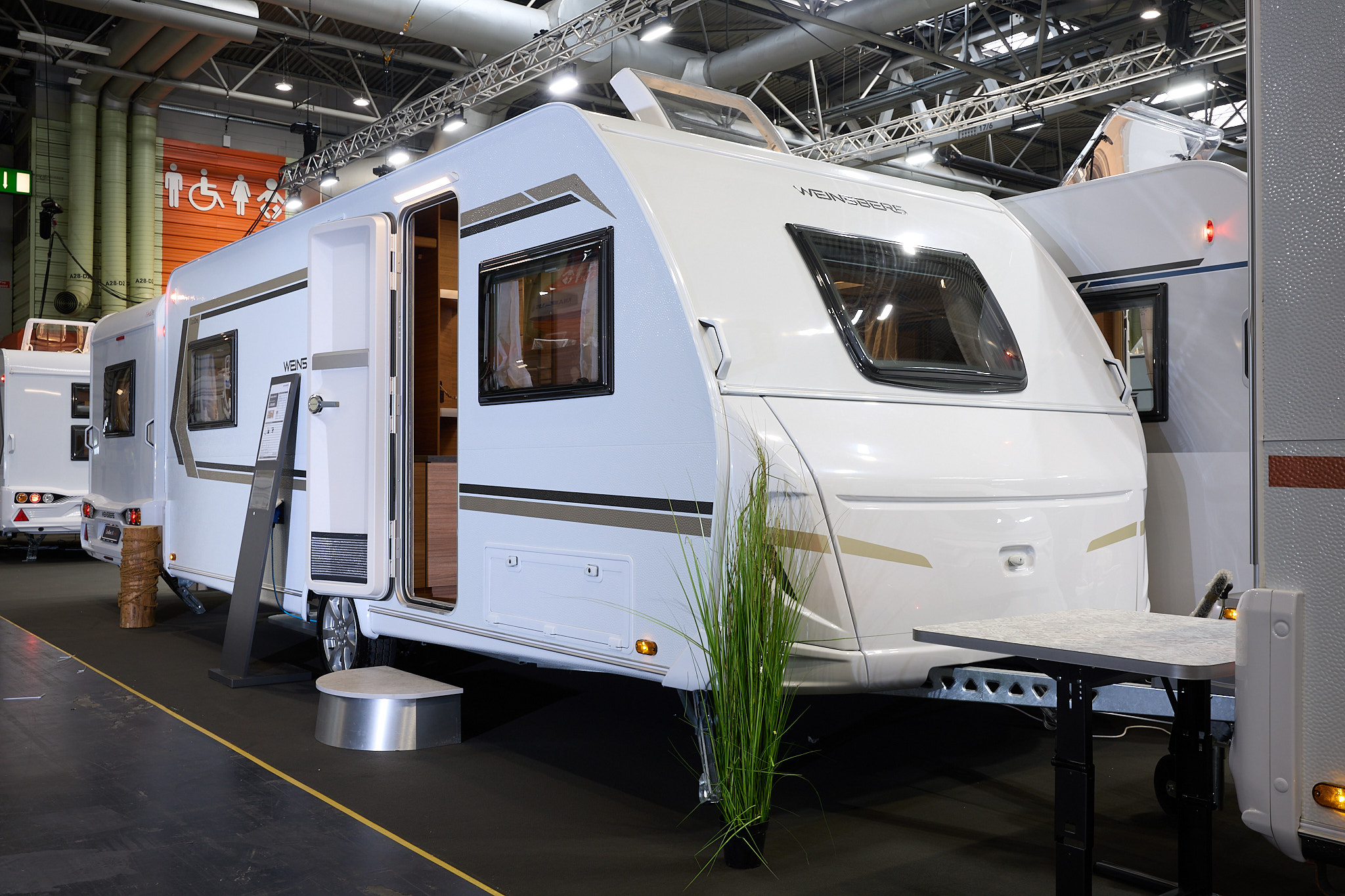 Weinsberg CaraOne 550 UK's exterior is white with brown and gold graphics.  The door is open and there is a step to enable easy access to the interior.
