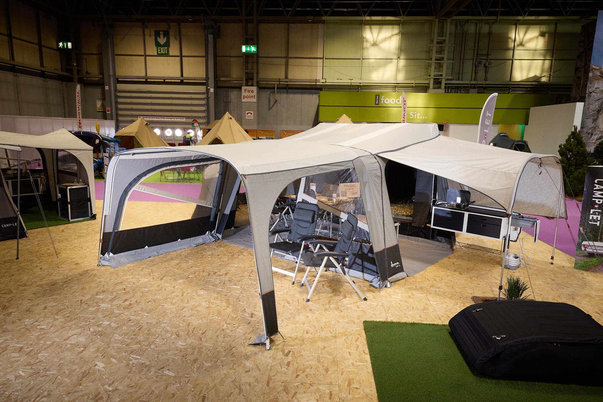 The Camp-Let Passion is manufactured of cream and brown canvas.  There is a separate annex for the kitchen.  The doors are open revealing the interior.  There are two camping chairs outside the main tent.  