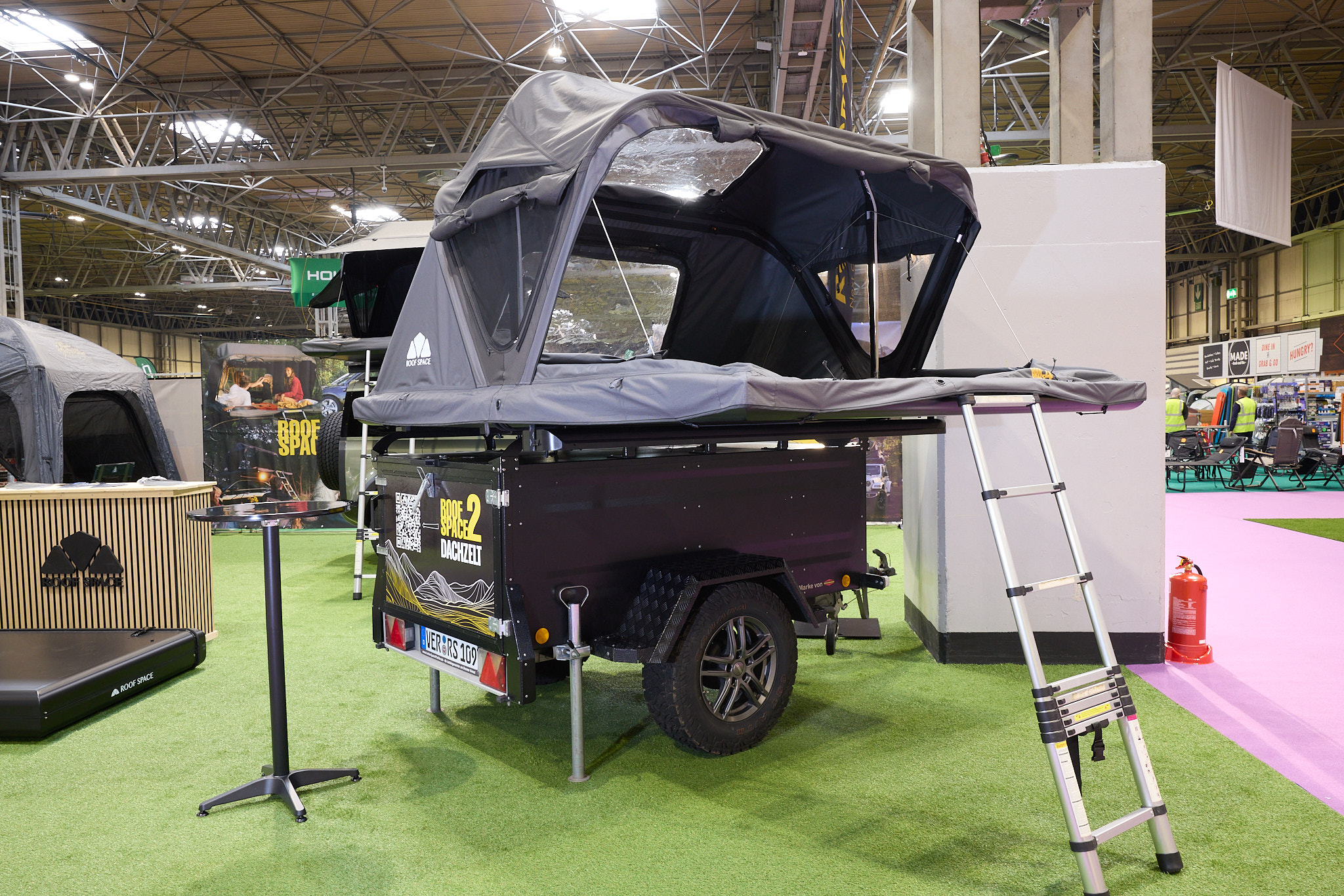 The Roof Space 2 is fully extended on a trailer.  The canvas is pale grey.  There is a platform with a sturdy ladder to gain easy access.