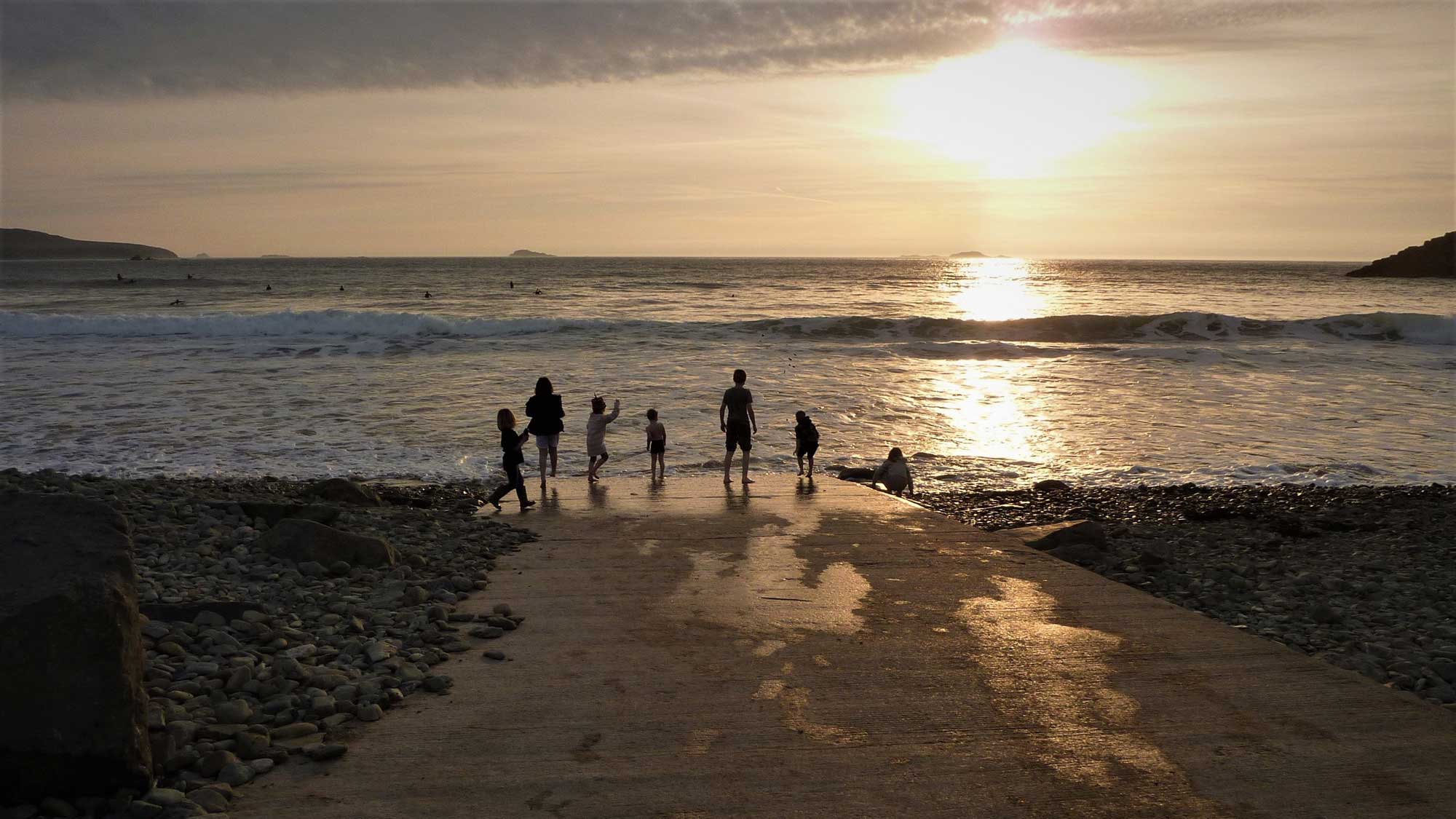 Sunset looking out onto the sea from the beach with a family of at the waters edge