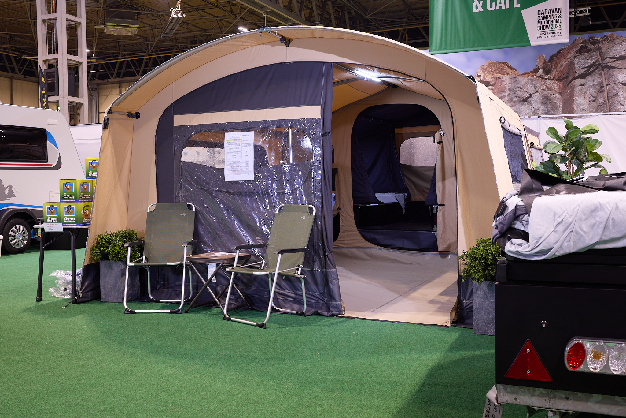 The Trigano Camplair S has yellow canvas with a brown canvas front.  The exterior door is open.  There are two camping chairs outside the tent.