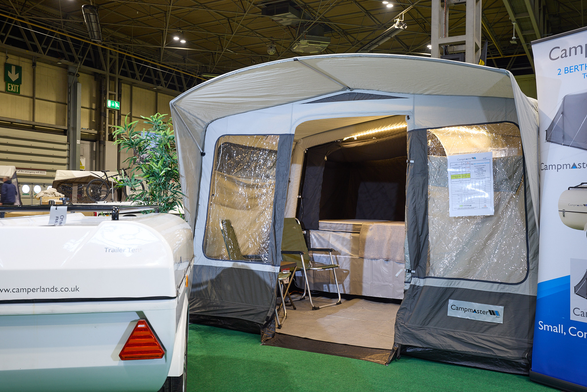 Campmaster 1000 LX has cream and brown canvas.  The doors are open revealing the interior.  There are two camping chairs inside the main tent.  The folded unit, in white, is to the left.
