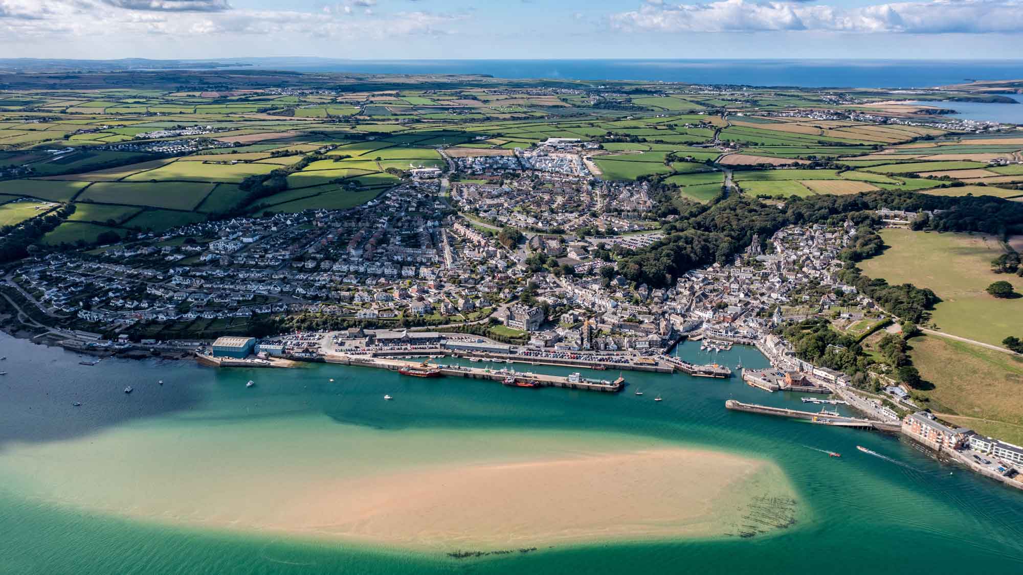 Aerial view of Padstow showing the clear sea that meets the town with a large sandbank rising up through the waters