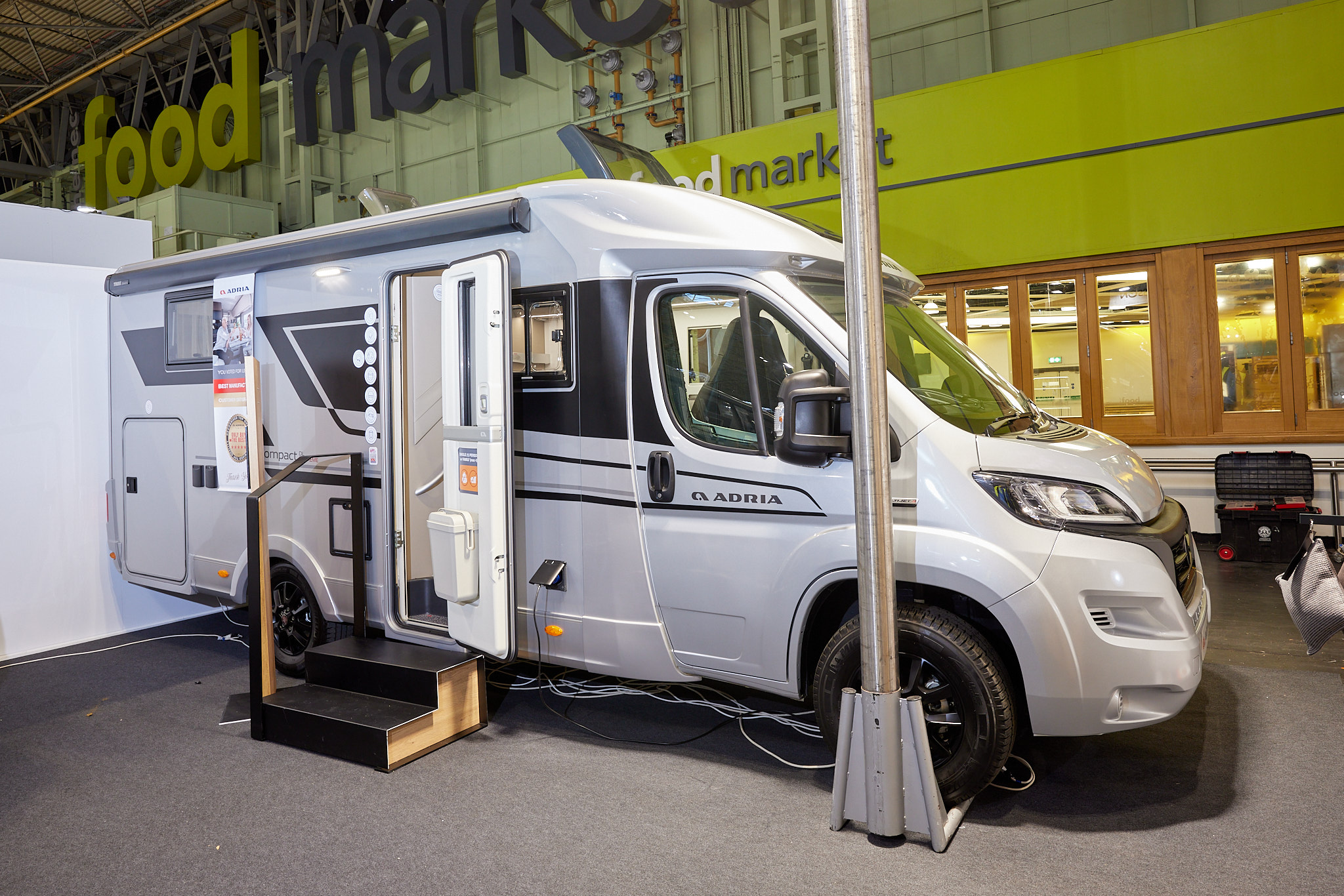 Adria Compact Supreme DL exterior, the motorhome is white with grey decals, the habitation door is open showing into the interior, with a double step to gain easy access. The roof lights are fully open.