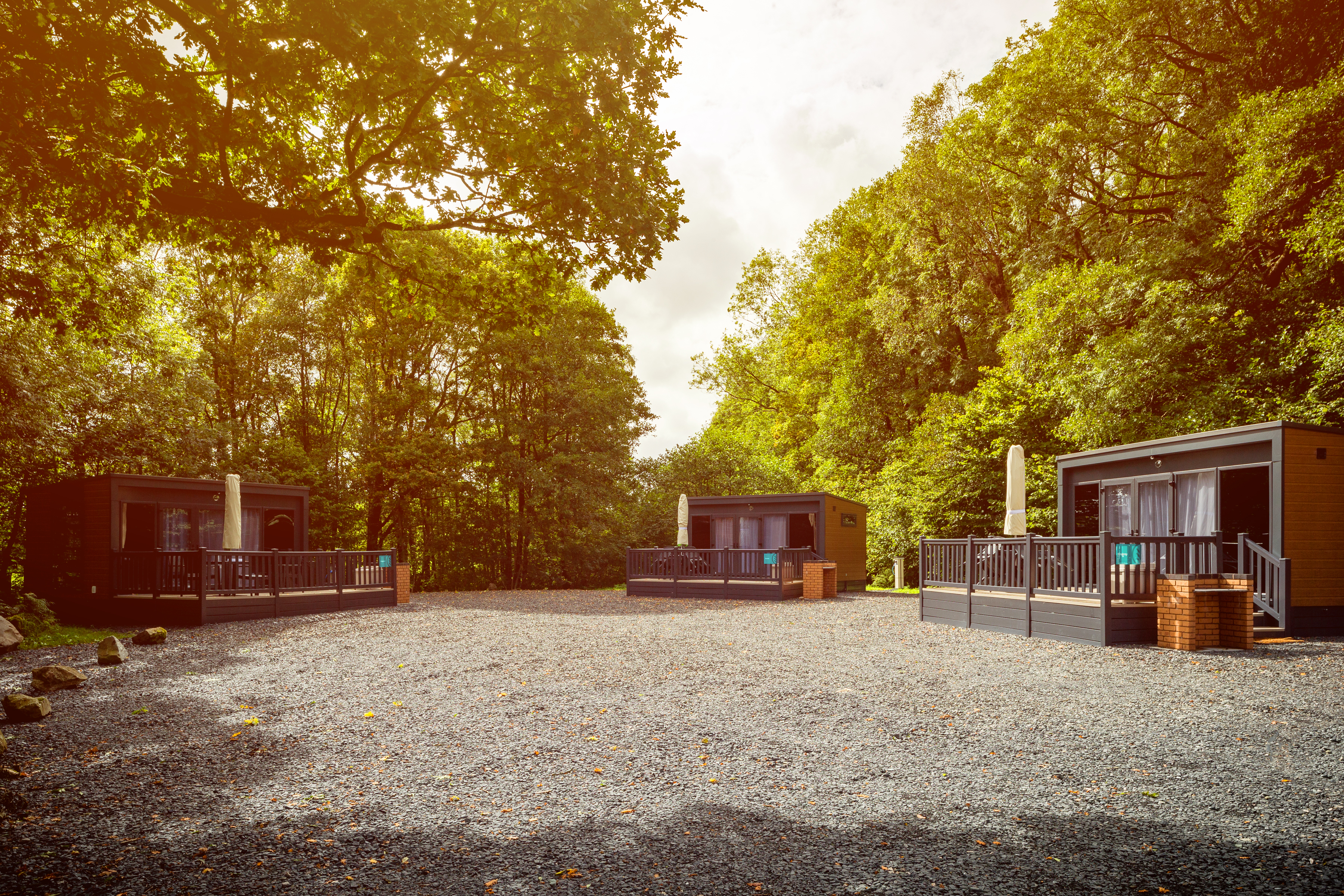 Three glamping pods on gravel area under green trees