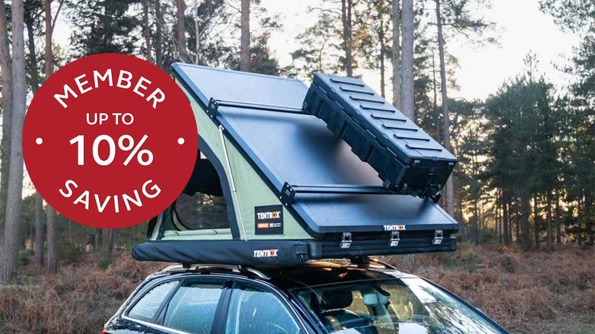 Car with a green roof tent and trees in the background